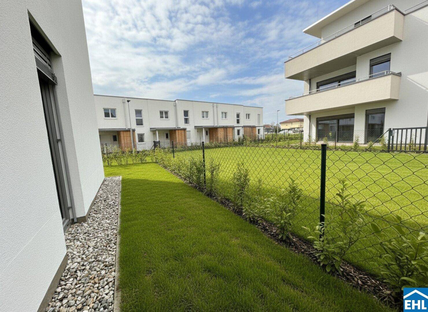Gepflegter Rasenbereich mit junger Bepflanzung und Blick auf moderne Reihenhäuser im Hintergrund.
