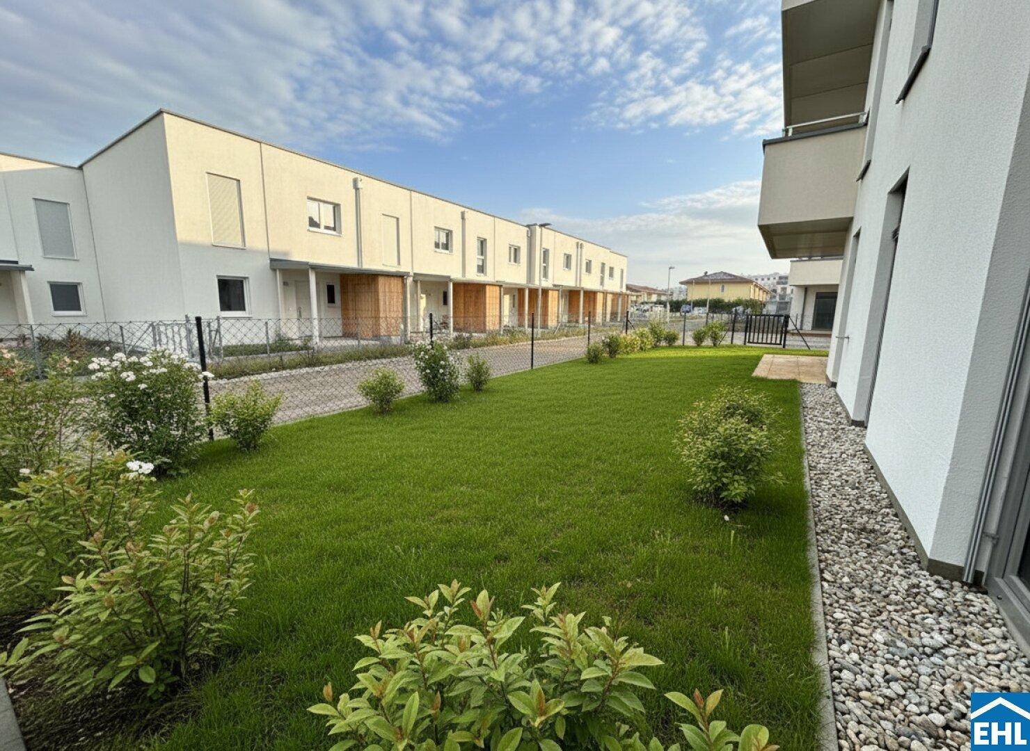 Grüner Gartenbereich mit Rasen und Sträuchern, umgeben von einer modernen Wohnsiedlung.
