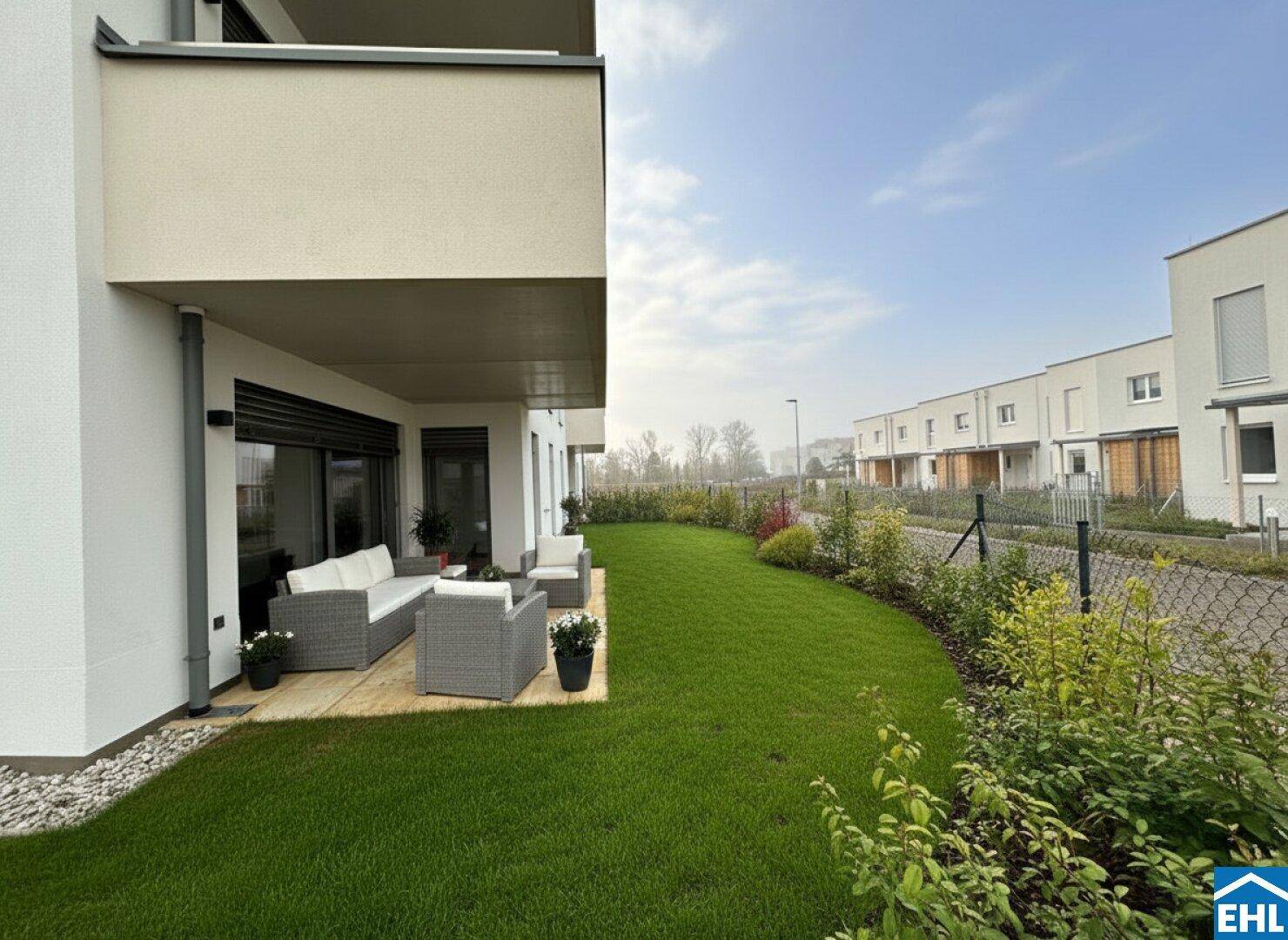 Möblierte Terrasse mit Sitzgelegenheiten und angrenzendem Rasenbereich in einer modernen Wohnanlage.