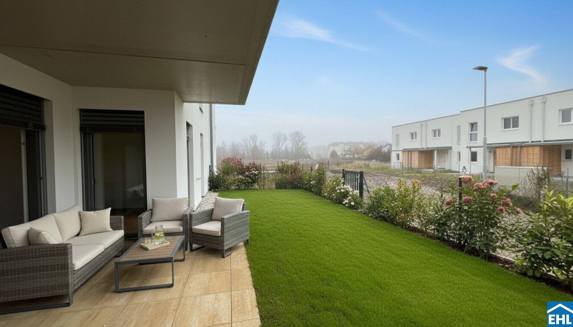 Gemütliche Terrasse mit Sitzgelegenheiten und angrenzendem Rasenbereich, umgeben von Grün.