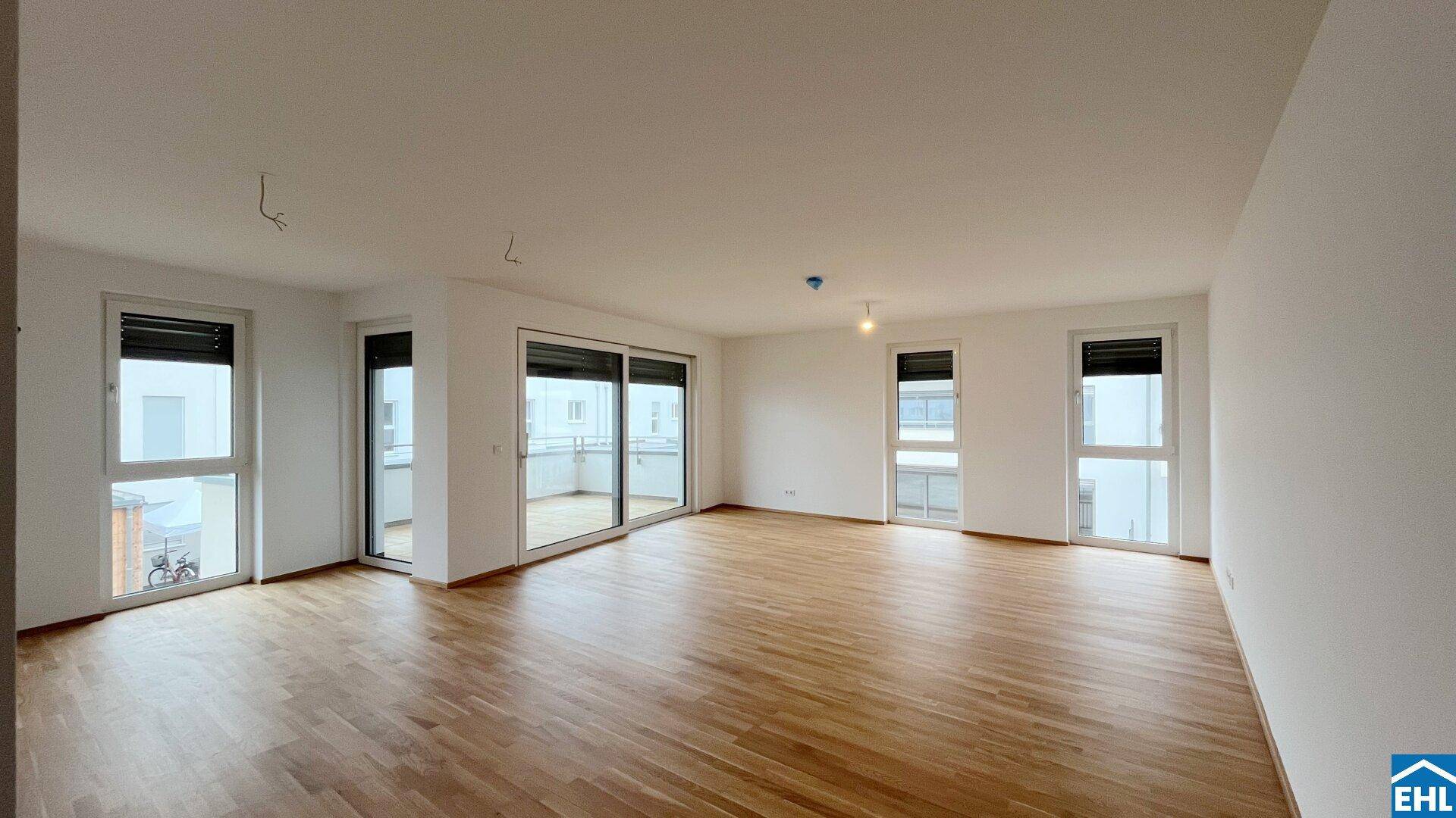 Heller, unmöblierter Wohnbereich mit mehreren Fenstern und Zugang zu einem Balkon.
