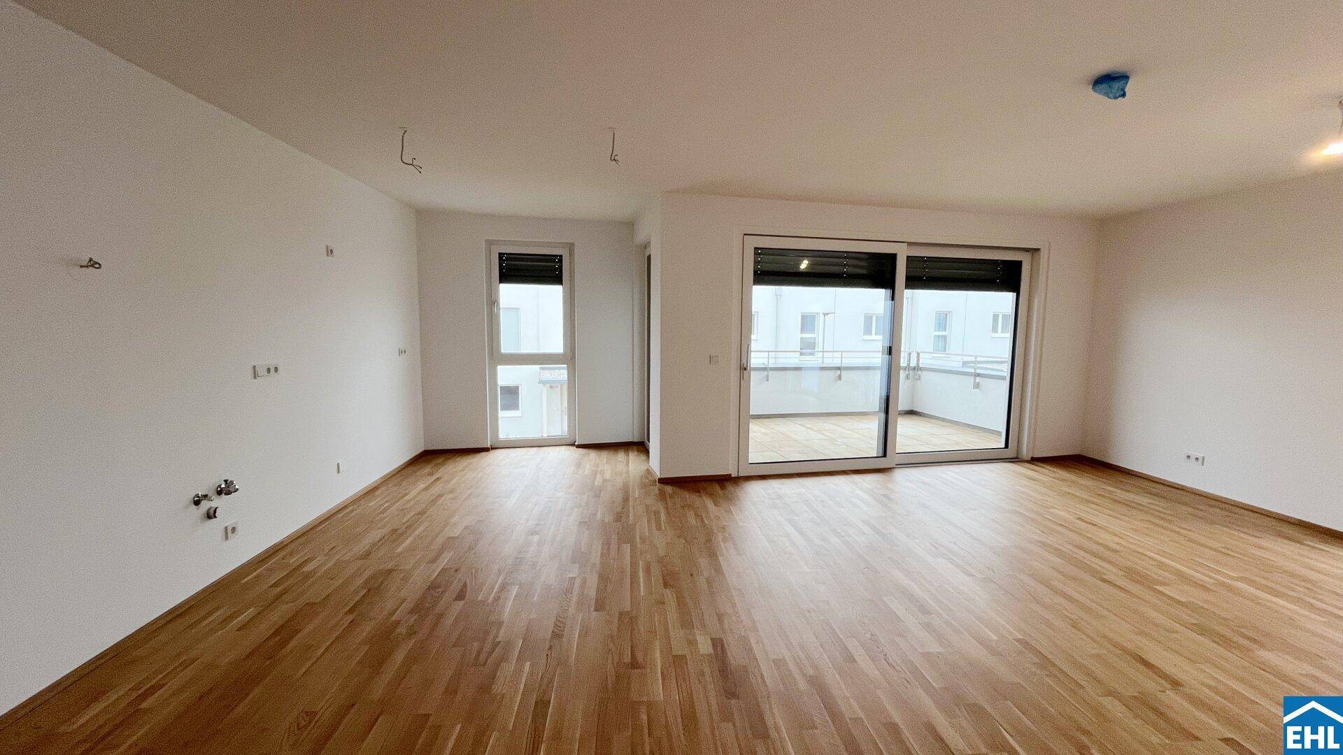 Geräumiger, leerer Wohnbereich mit hellem Parkettboden und großzügigem Balkonzugang.
