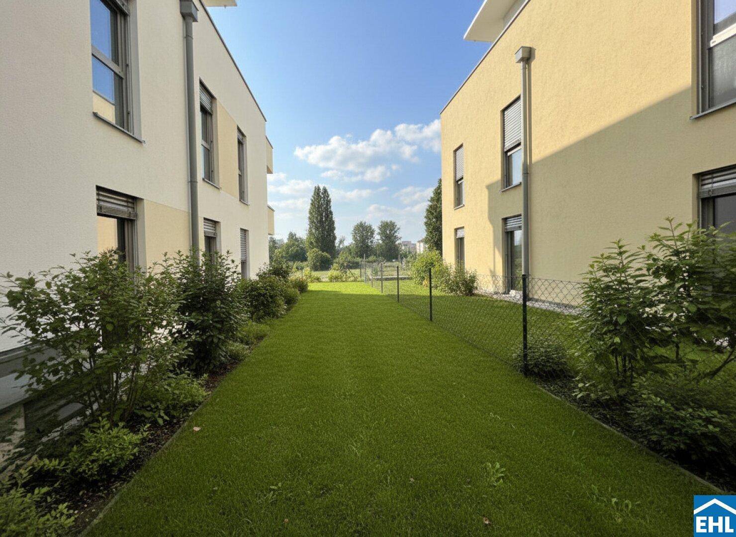 Gepflegte Grünfläche zwischen modernen Wohngebäuden unter blauem Himmel.