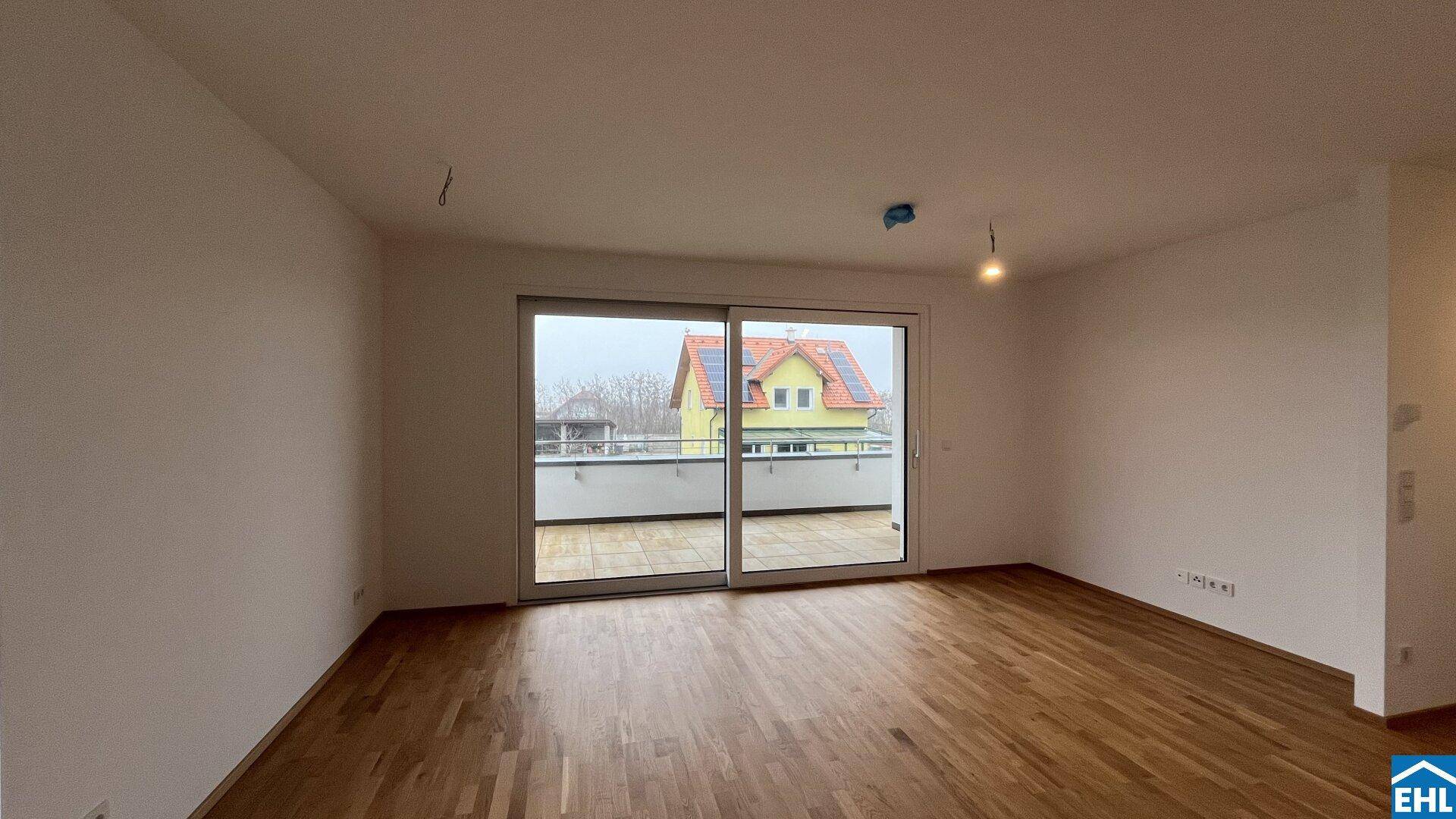 Lichtdurchfluteter Raum mit Parkettboden und breiter Glasfront, die den Blick nach draußen freigibt.