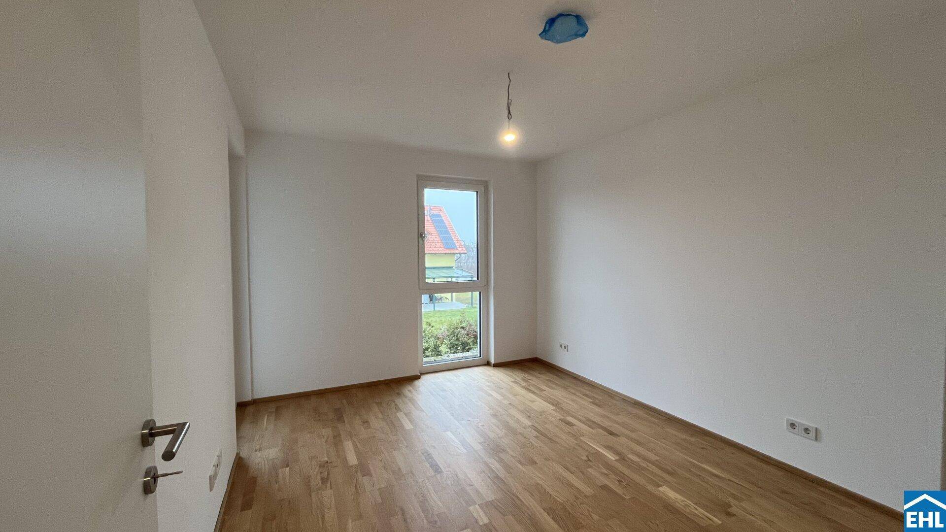 Helles Schlafzimmer mit Parkettboden und einem Fenster, das viel Tageslicht hereinlässt.