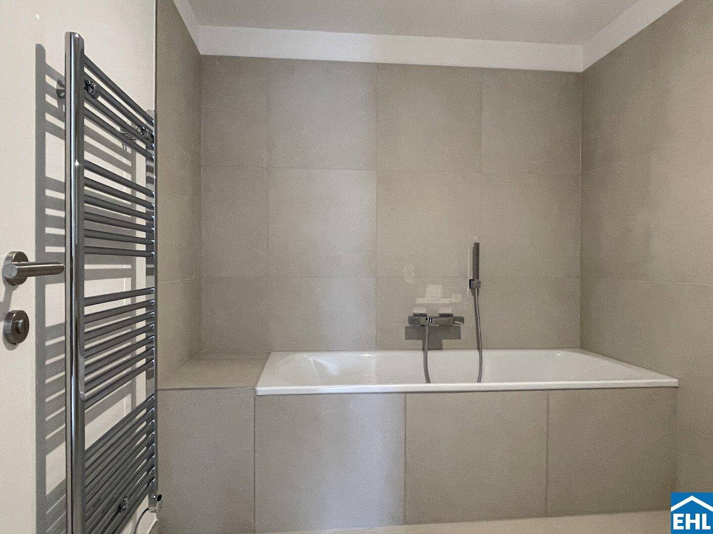 Helles Badezimmer mit Badewanne, beheiztem Handtuchhalter und modernen grauen Fliesen.