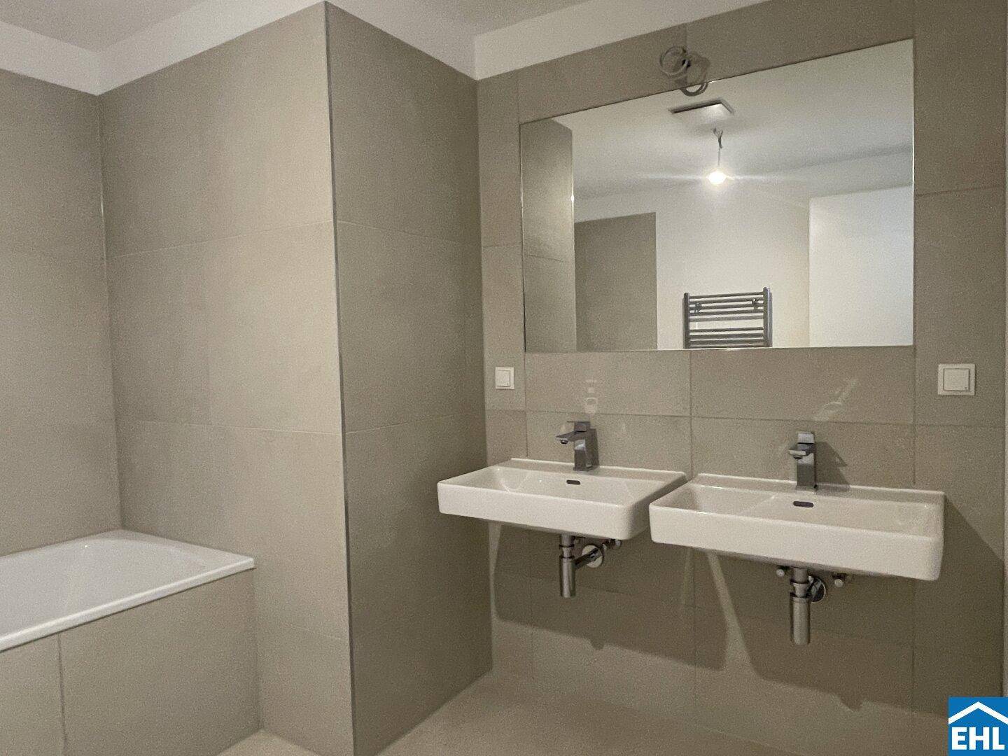 Modernes Badezimmer mit Doppelwaschbecken, Badewanne und großen grauen Fliesen.