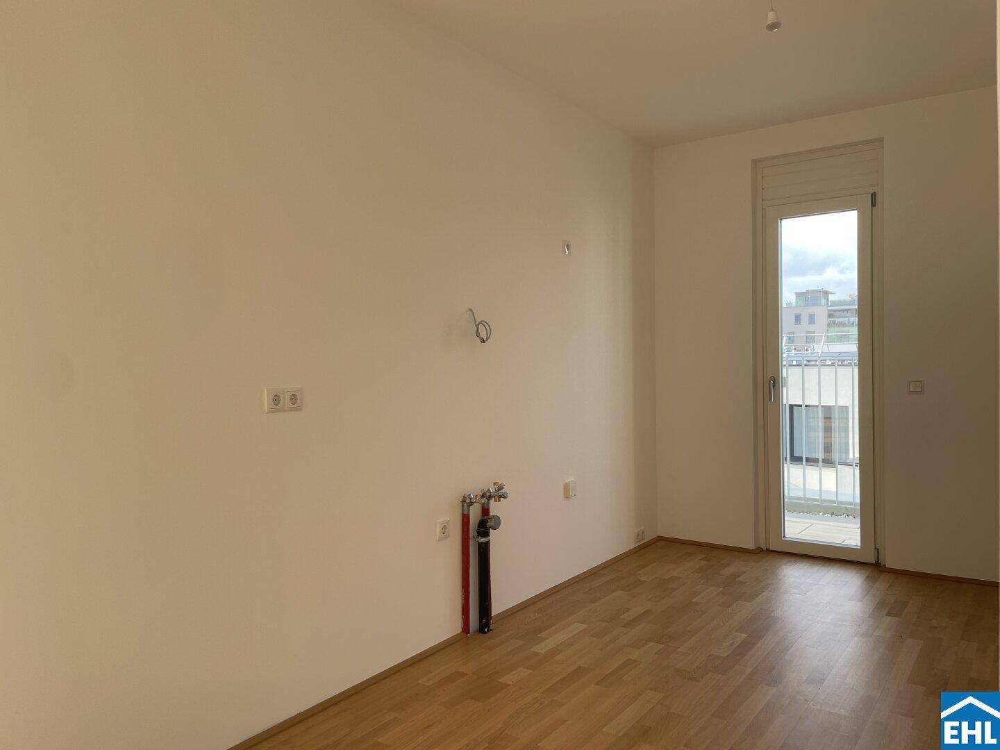Leerer Küchenbereich mit Anschlüssen für Spüle und Geräte, bereit für die Installation einer Einbauküche.