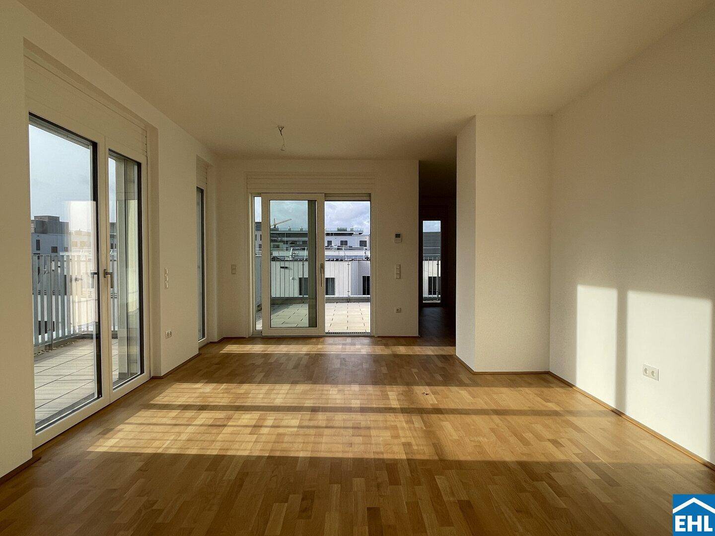 Geräumiger, unmöblierter Raum mit Holzboden und Zugang zu einer großen Terrasse.