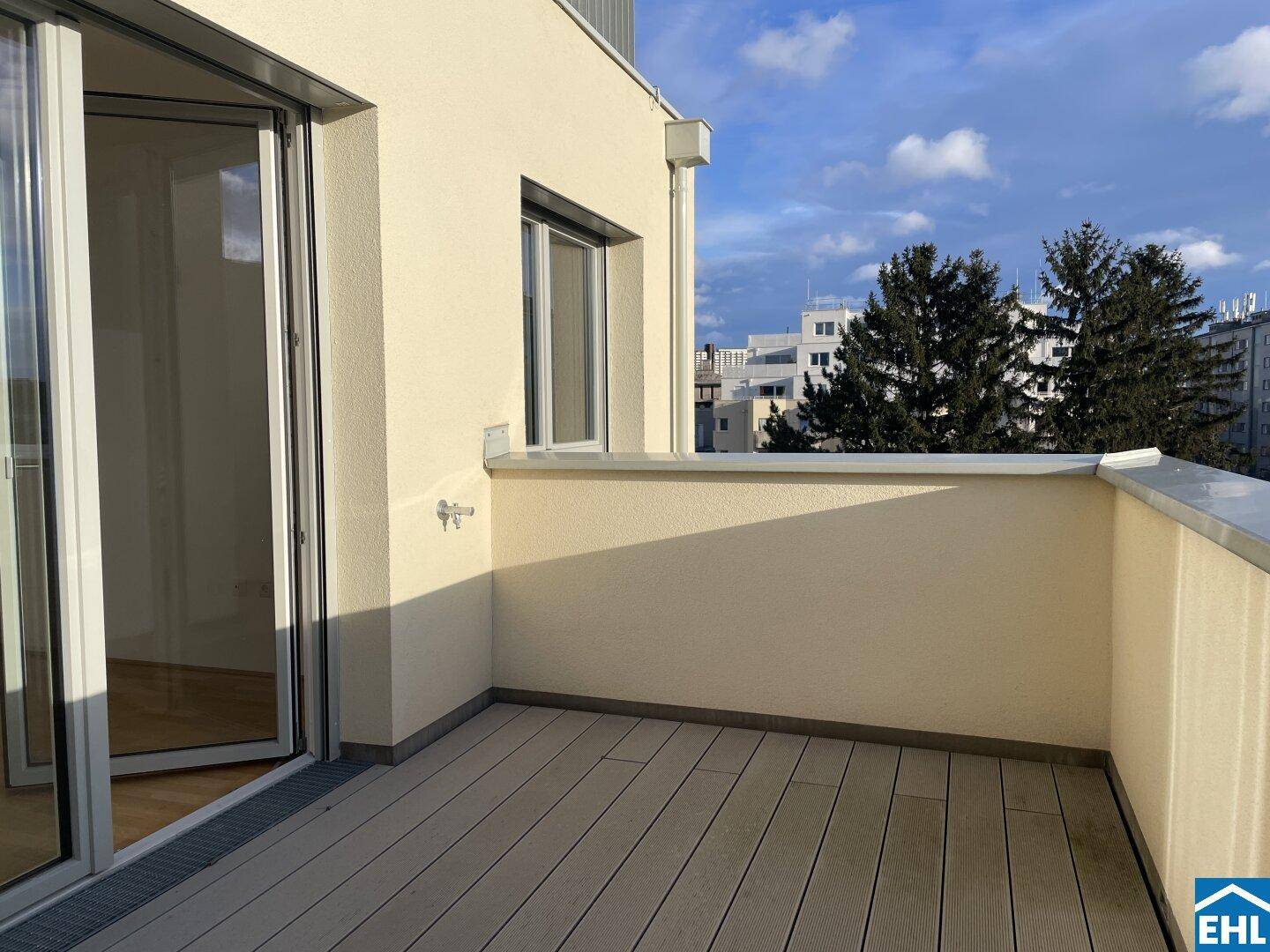 Geräumiger Balkon mit Holzdielen und Blick auf die umliegende Stadtlandschaft und Bäume.
