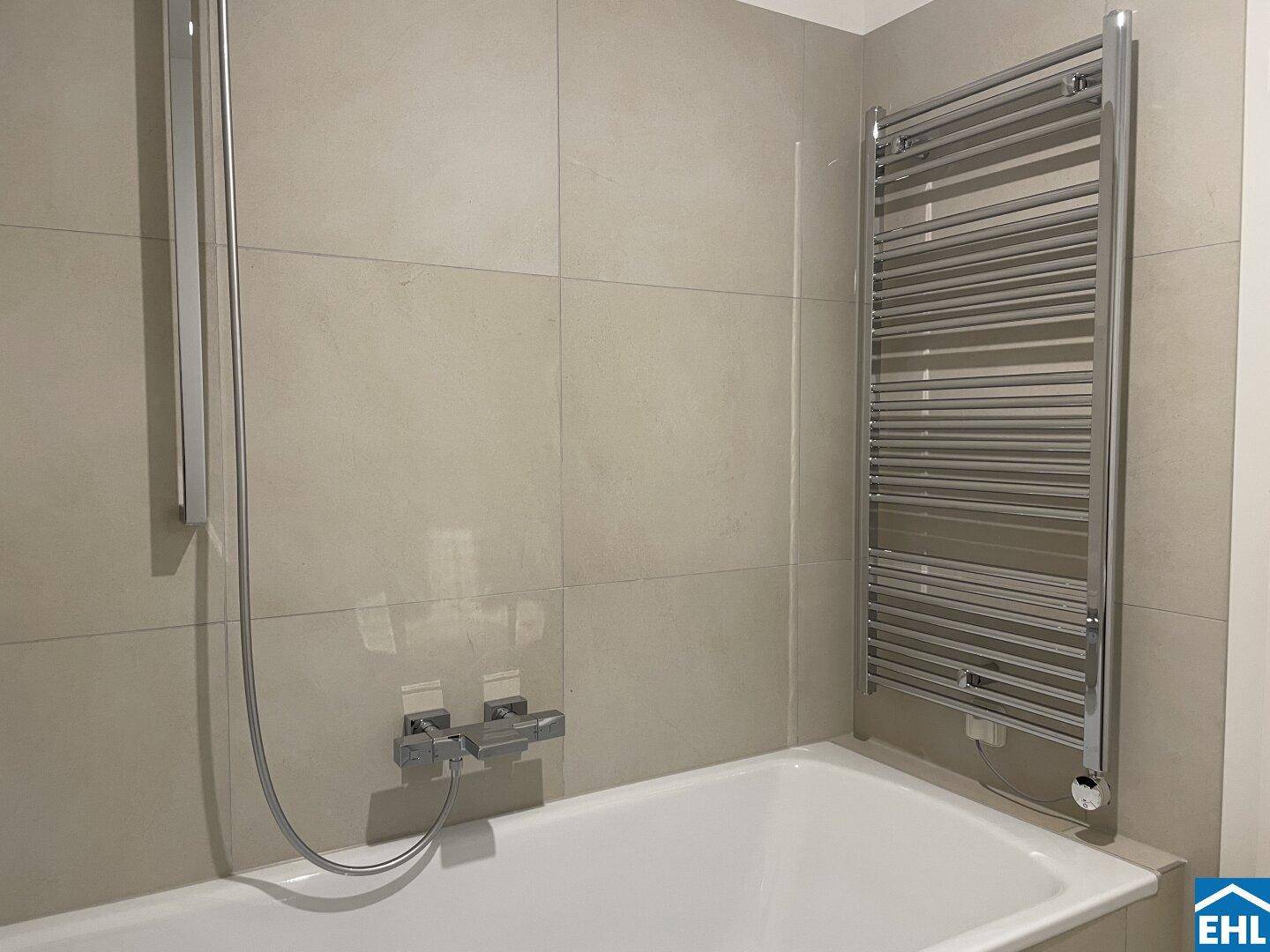 Modernes Badezimmer mit Badewanne, Duscharmatur und beheiztem Handtuchhalter an der Wand.