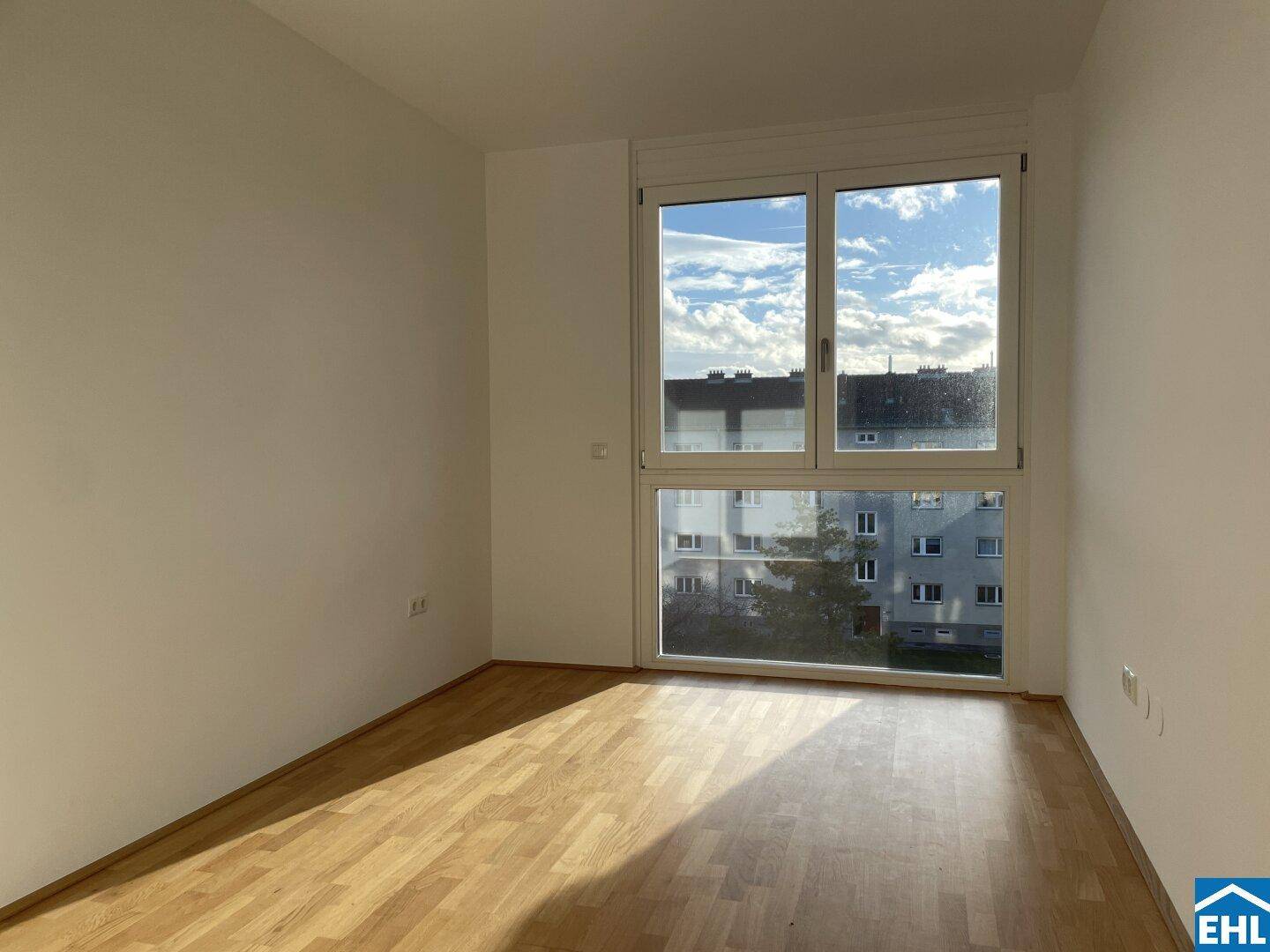 Leerer Raum mit großen Fenstern und Parkettboden, ideal für individuelle Gestaltung und viel Tageslicht.