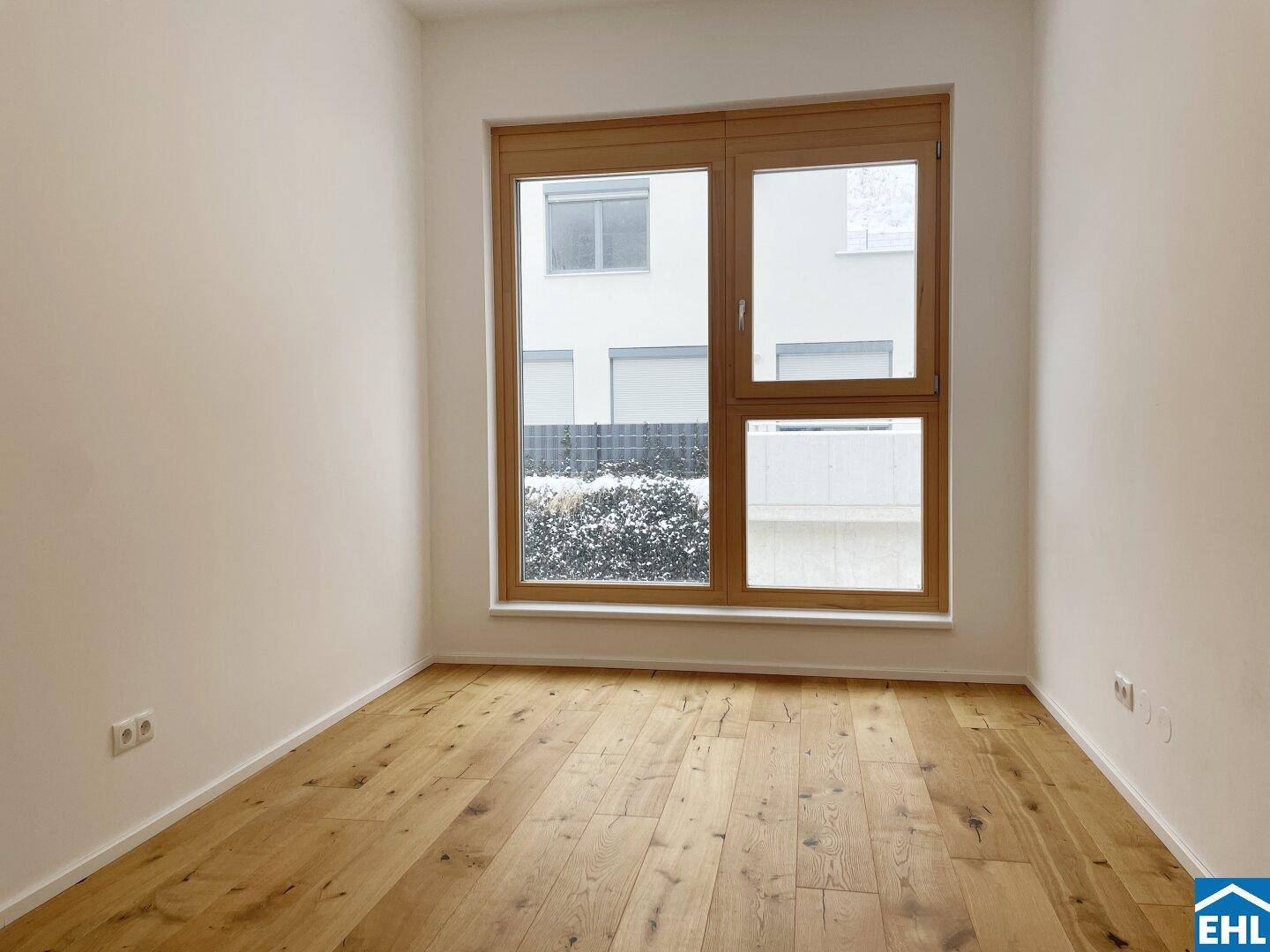 Leeres Zimmer mit Holzboden und großem Fenster, ideal als Schlaf- oder Arbeitszimmer.