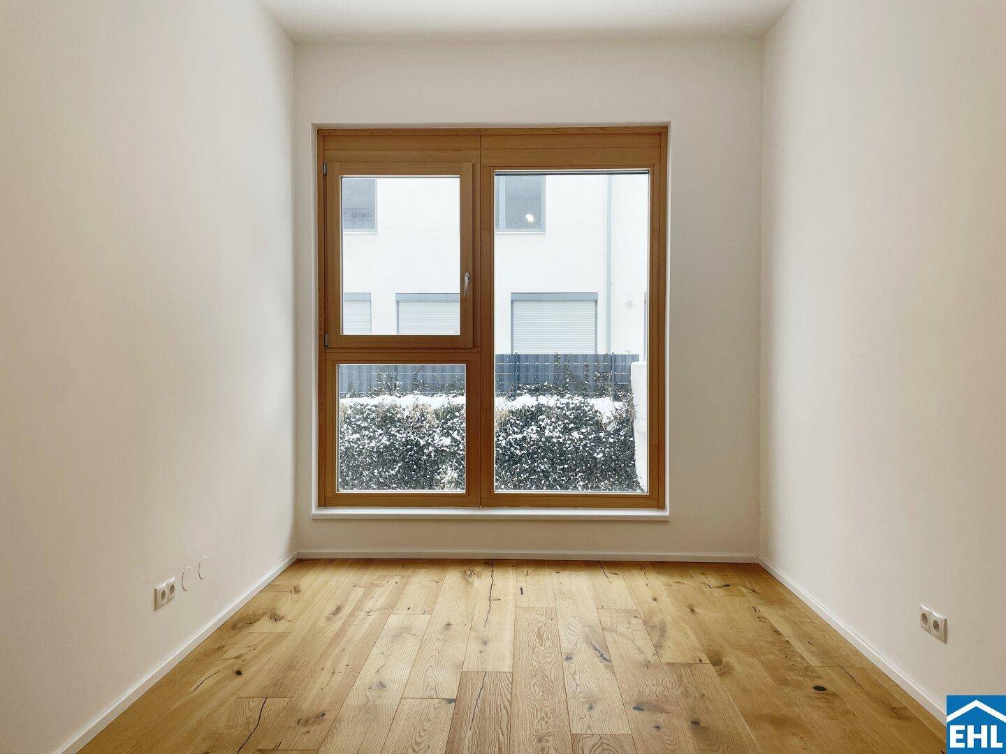 Helles Schlafzimmer mit Holzboden und großem Fenster mit Blick auf die Umgebung.