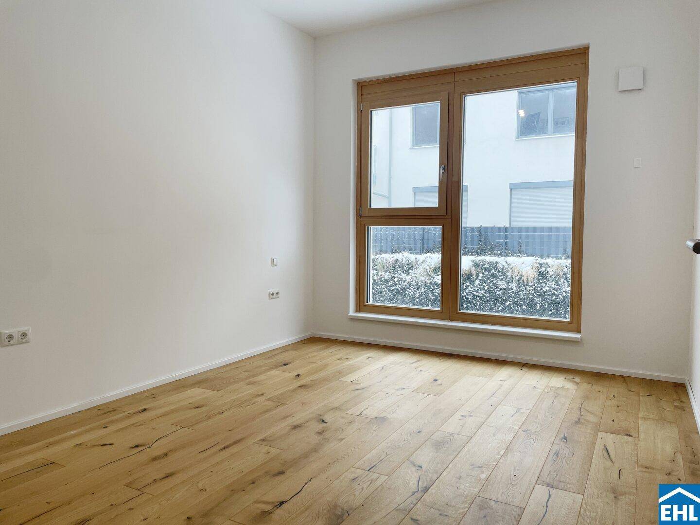 Helles leeres Zimmer mit Holzboden und großem Fenster, bereit zur individuellen Gestaltung.