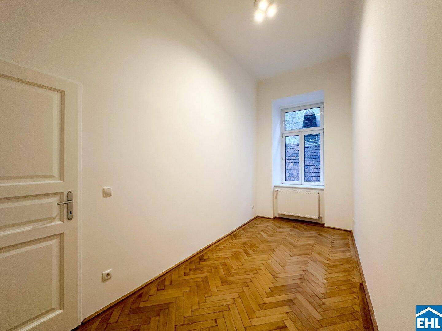 Geräumiges Zimmer mit elegantem Fischgrätparkett und einer klassischen weißen Tür.