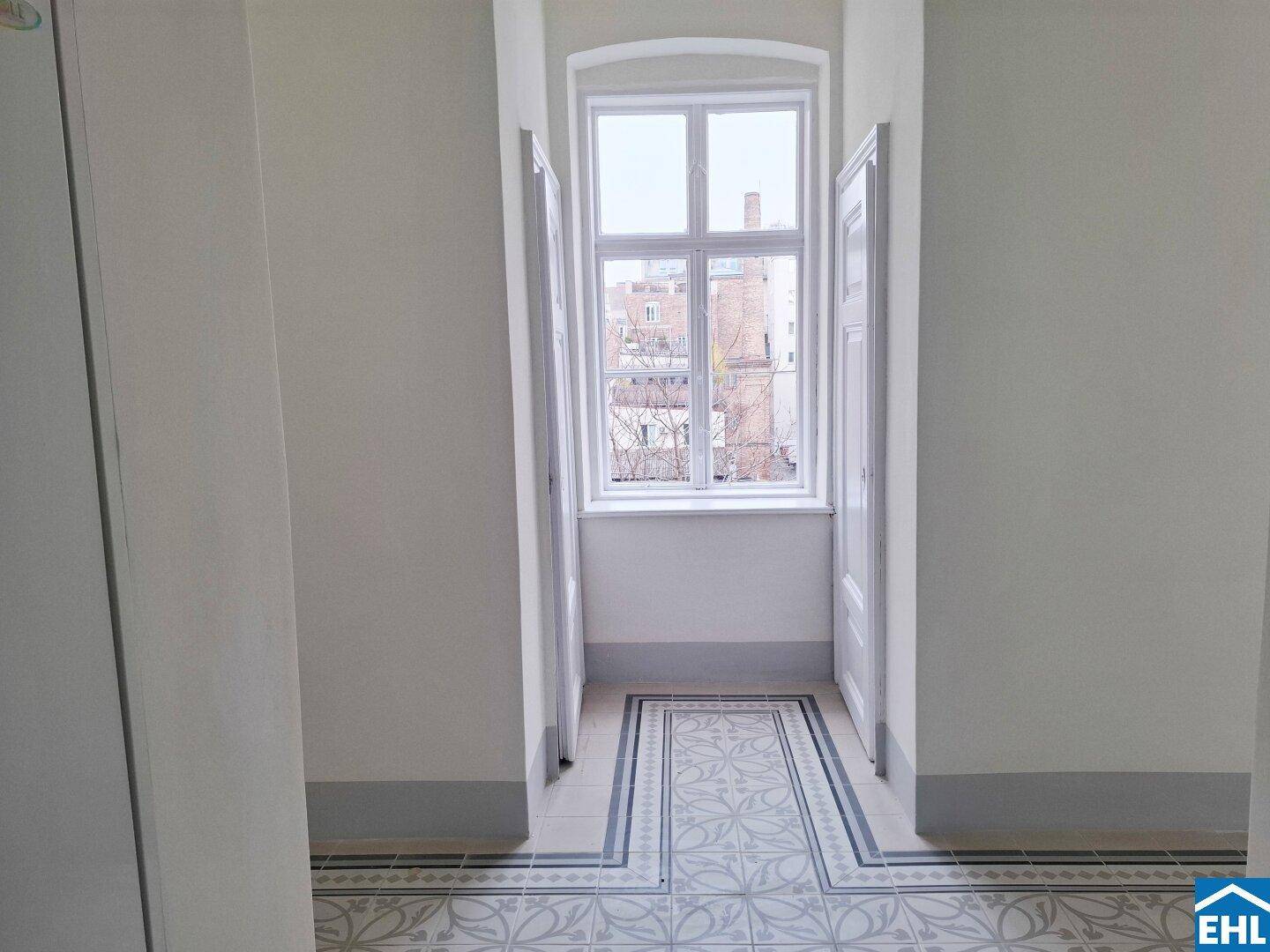Heller Flur mit dekorativen Fliesen und einem großen Fenster, das Tageslicht hereinlässt.
