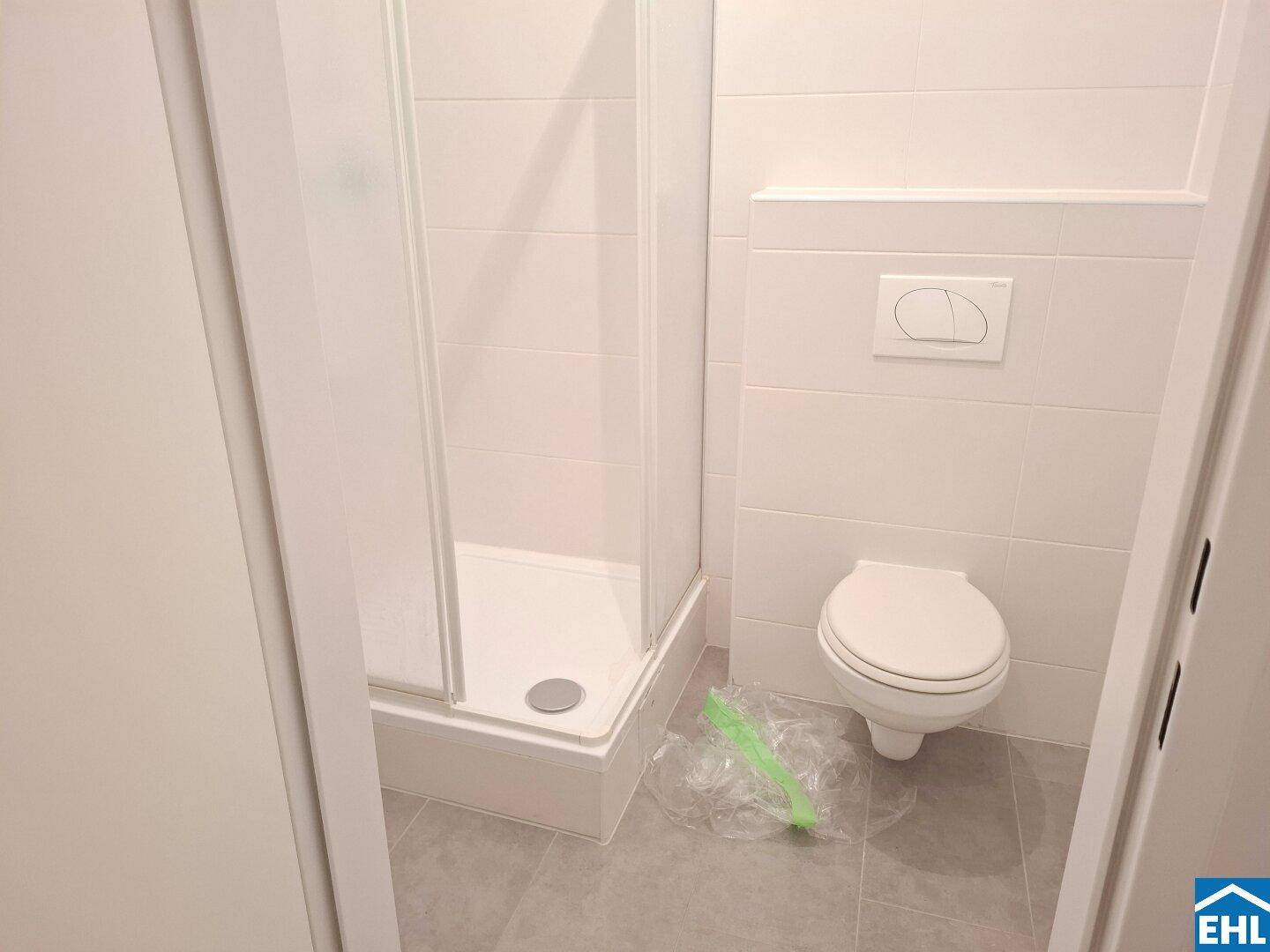 Modernes Badezimmer mit Duschkabine und wandhängendem WC, komplett gefliest.