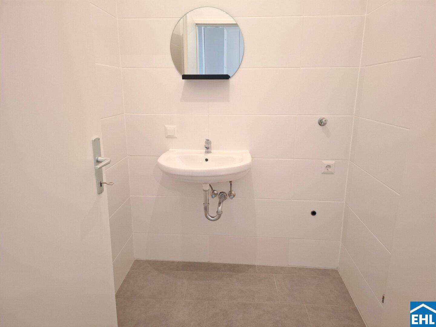 Helles Badezimmer mit modernem Waschbecken und rundem Spiegel über dem Waschtisch.