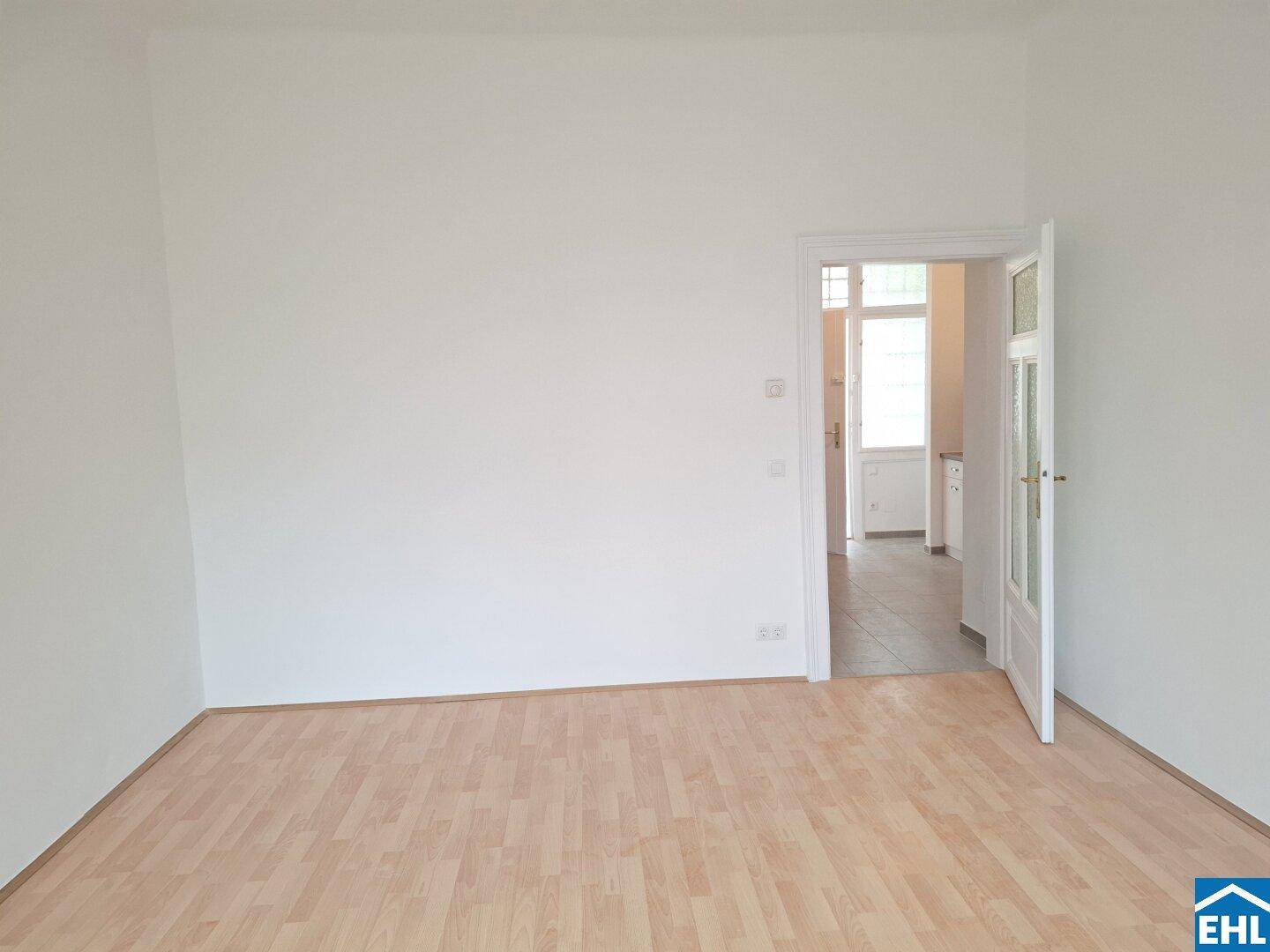 Geräumiger, leerer Raum mit Laminatboden und offener Tür zu einem weiteren Bereich.