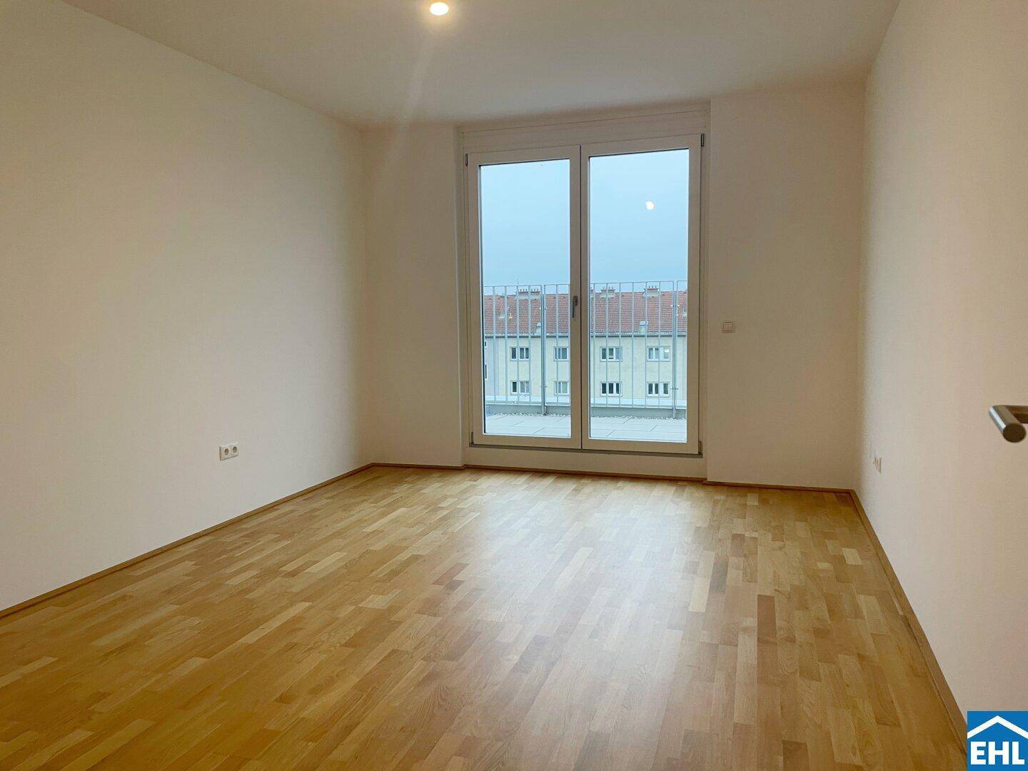 Geräumiger, heller Raum mit Parkettboden und Zugang zu einem französischen Balkon.