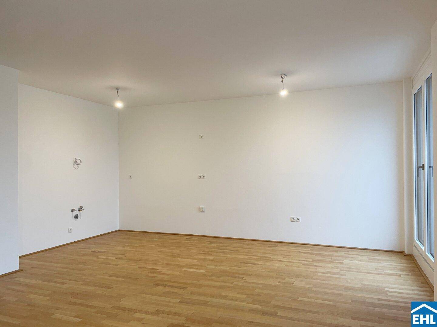 Heller, leerer Wohnbereich mit Parkettboden und großem Fenster, bereit für individuelle Gestaltung.