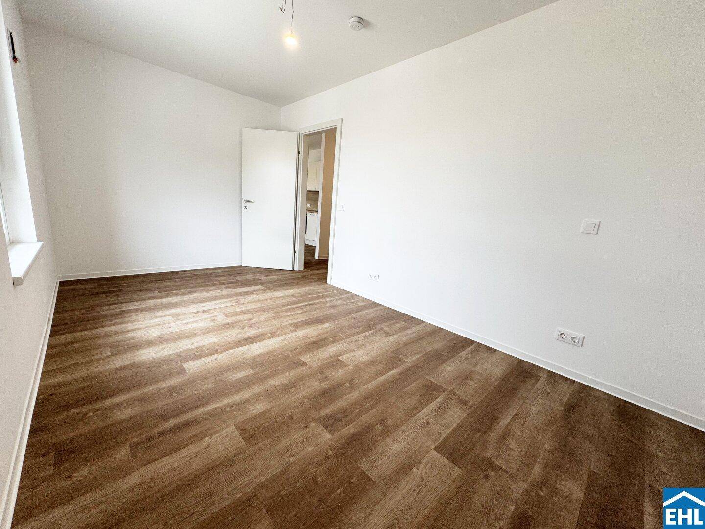 Leeres Zimmer mit Holzboden und weißen Wänden, ideal als Schlaf- oder Arbeitszimmer.