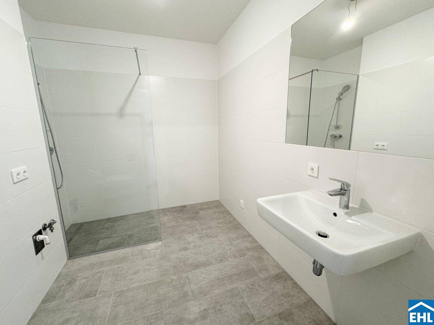 Helles Badezimmer mit modernem Waschtisch, großem Spiegel und geräumiger Dusche.