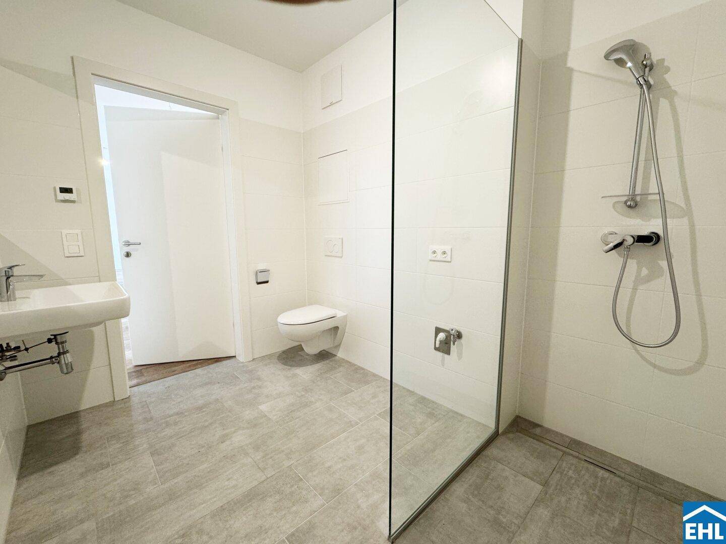 Modernes Badezimmer mit bodengleicher Dusche, Hänge-WC und hellen Fliesen.