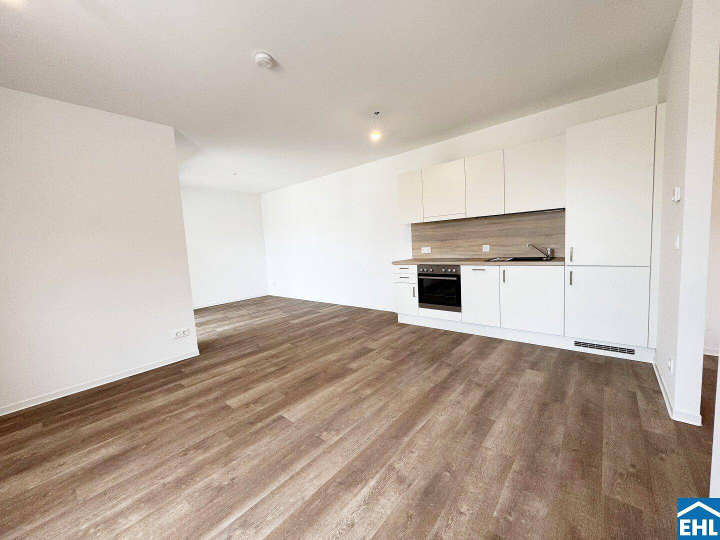 Geräumiger Wohnbereich mit moderner Einbauküche und hellem Laminatboden.