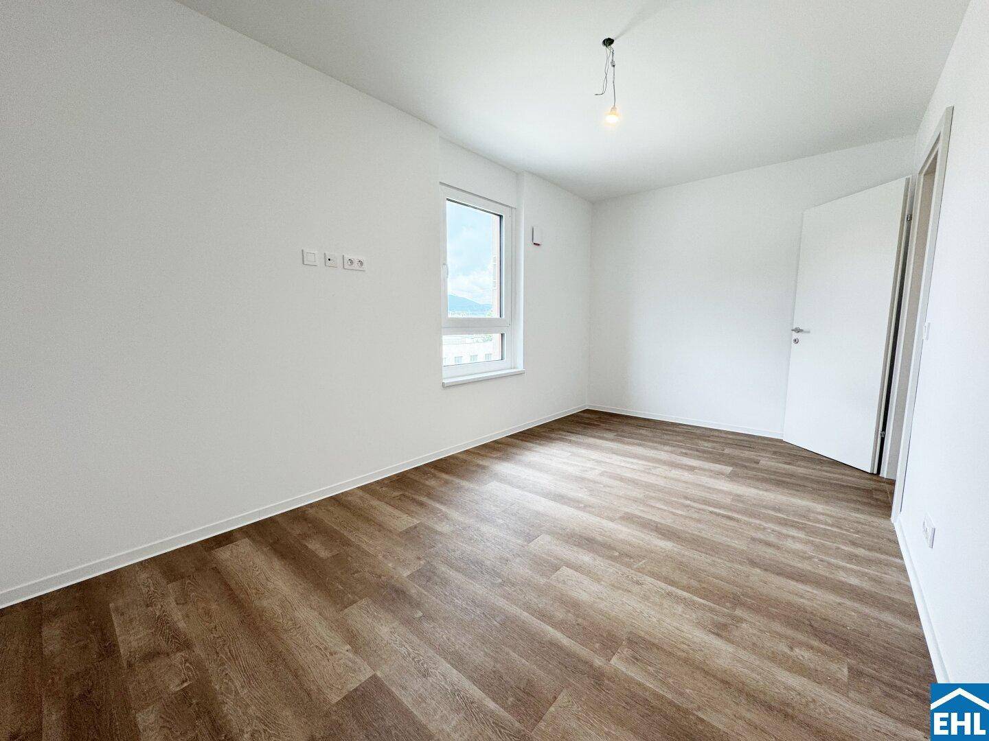 Helles Zimmer mit Fenster, Holzboden und weißen Wänden, bereit zur individuellen Gestaltung.