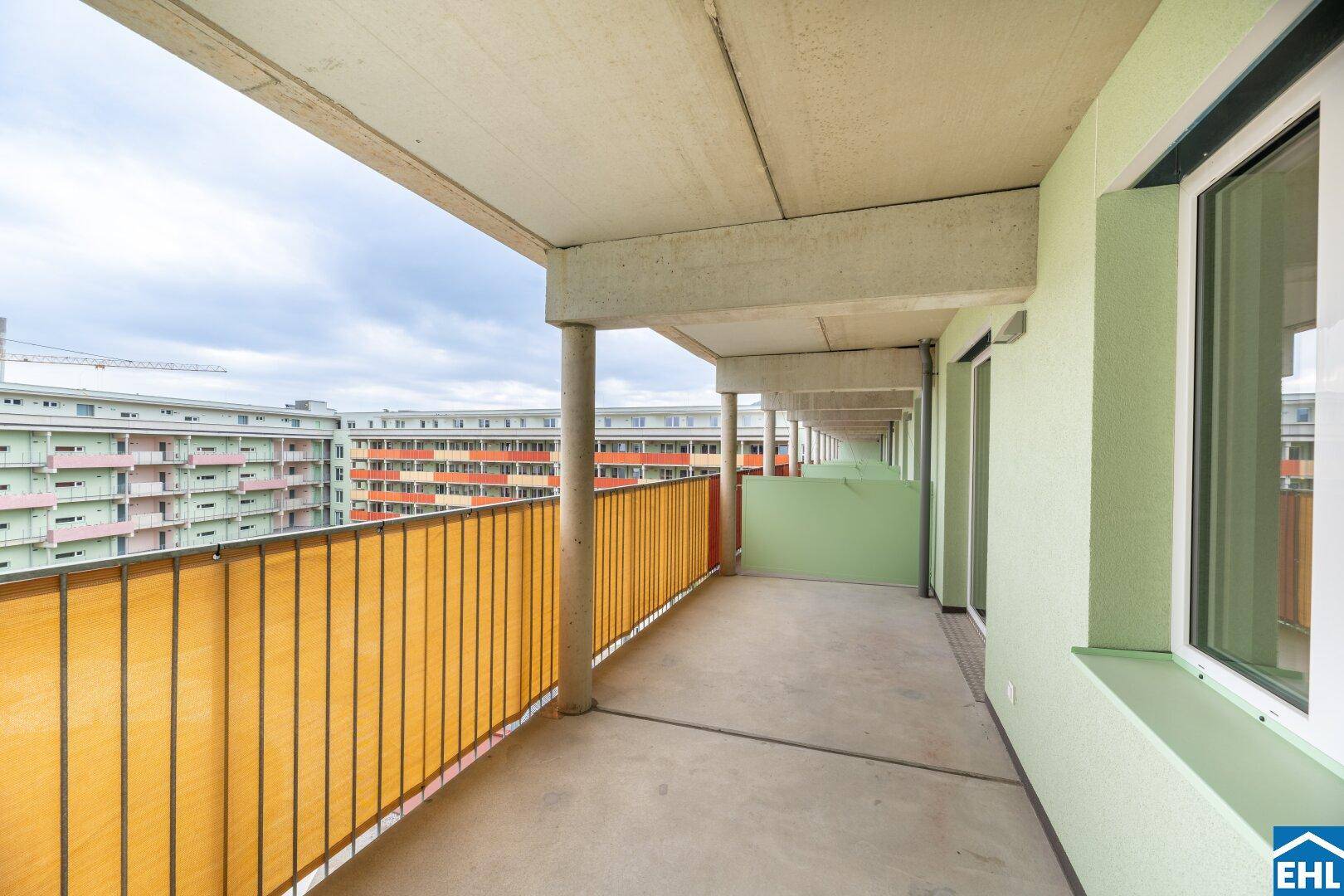 Langer Balkon mit Blick auf die umliegenden Wohngebäude und gelbem Sichtschutz.