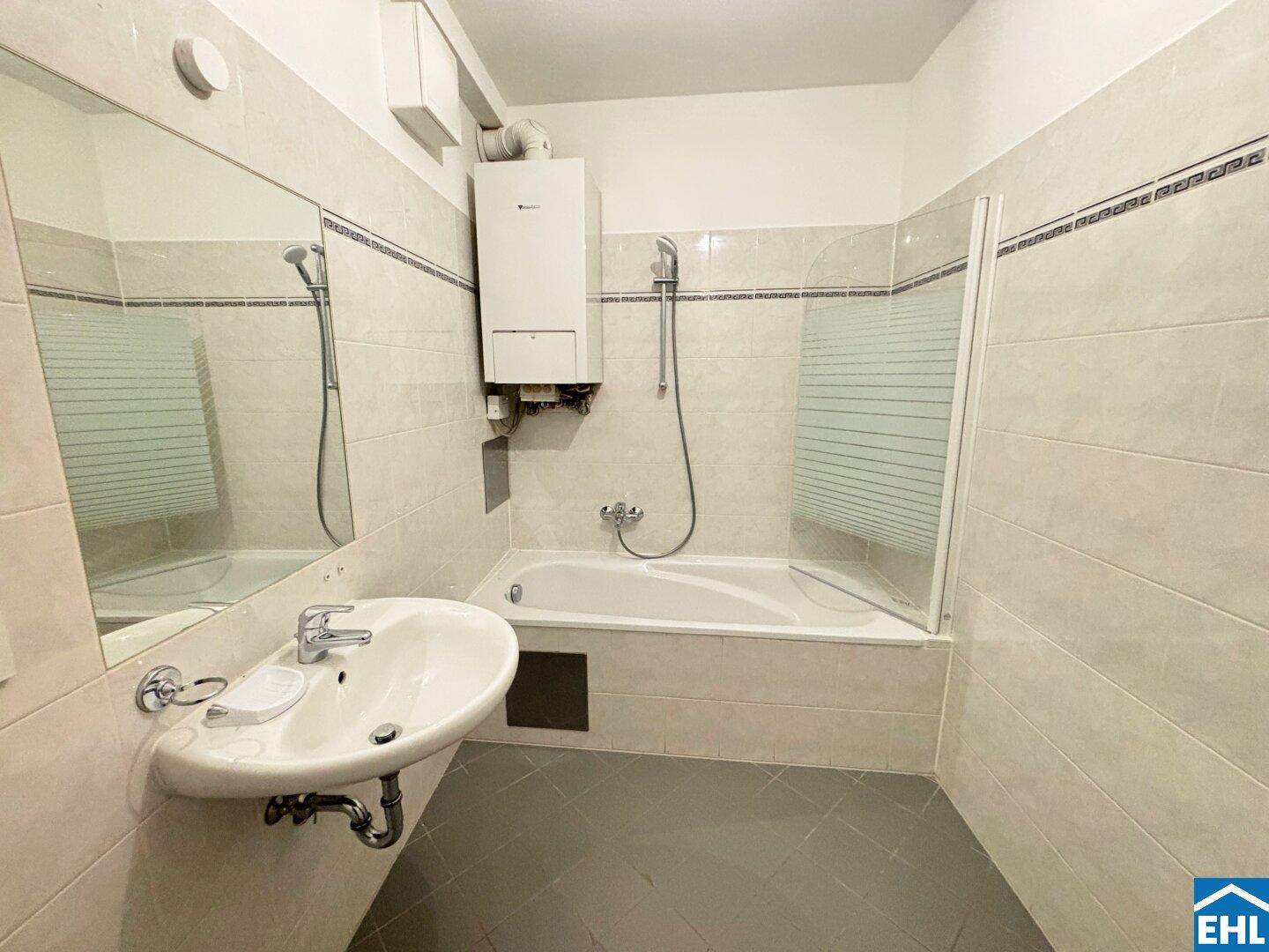 Gefliestes Badezimmer mit Badewanne, Waschbecken und Wandspiegel, inklusive Gastherme.
