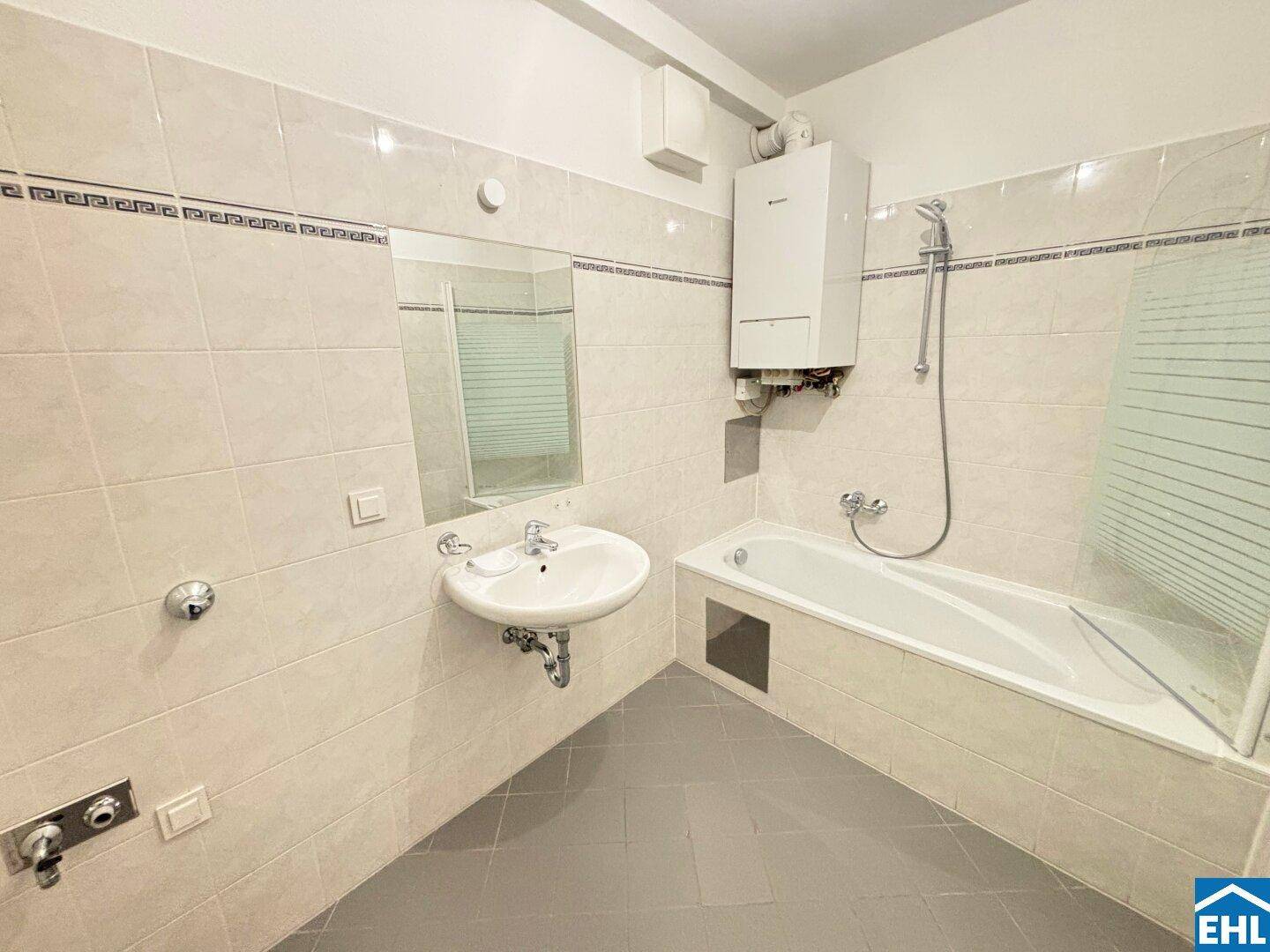 Funktionales Badezimmer mit hellen Fliesen, Badewanne mit Duschfunktion und Waschbecken.