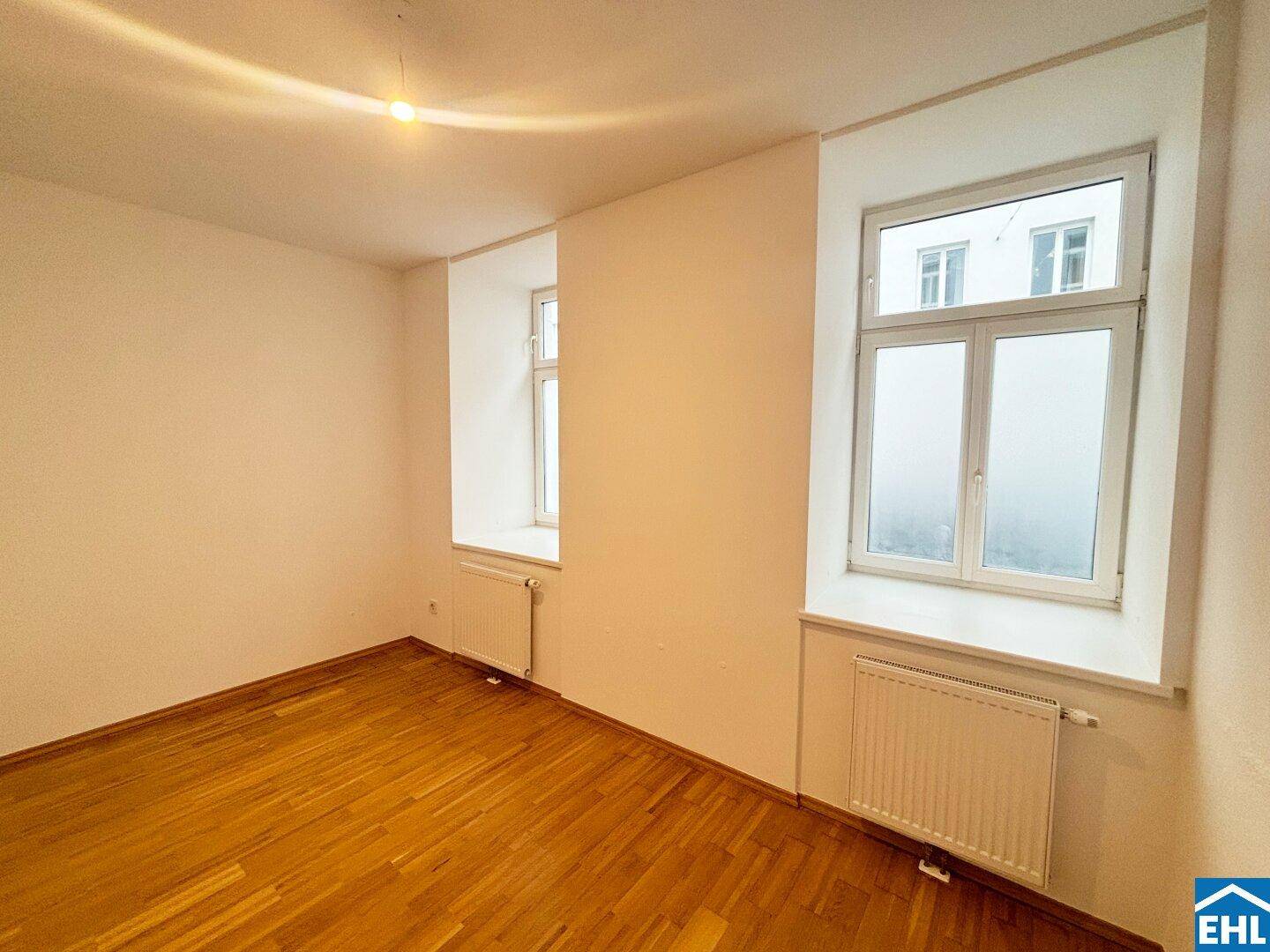 Helles Zimmer mit Parkettboden und zwei Fenstern, geeignet als Schlaf- oder Arbeitszimmer.