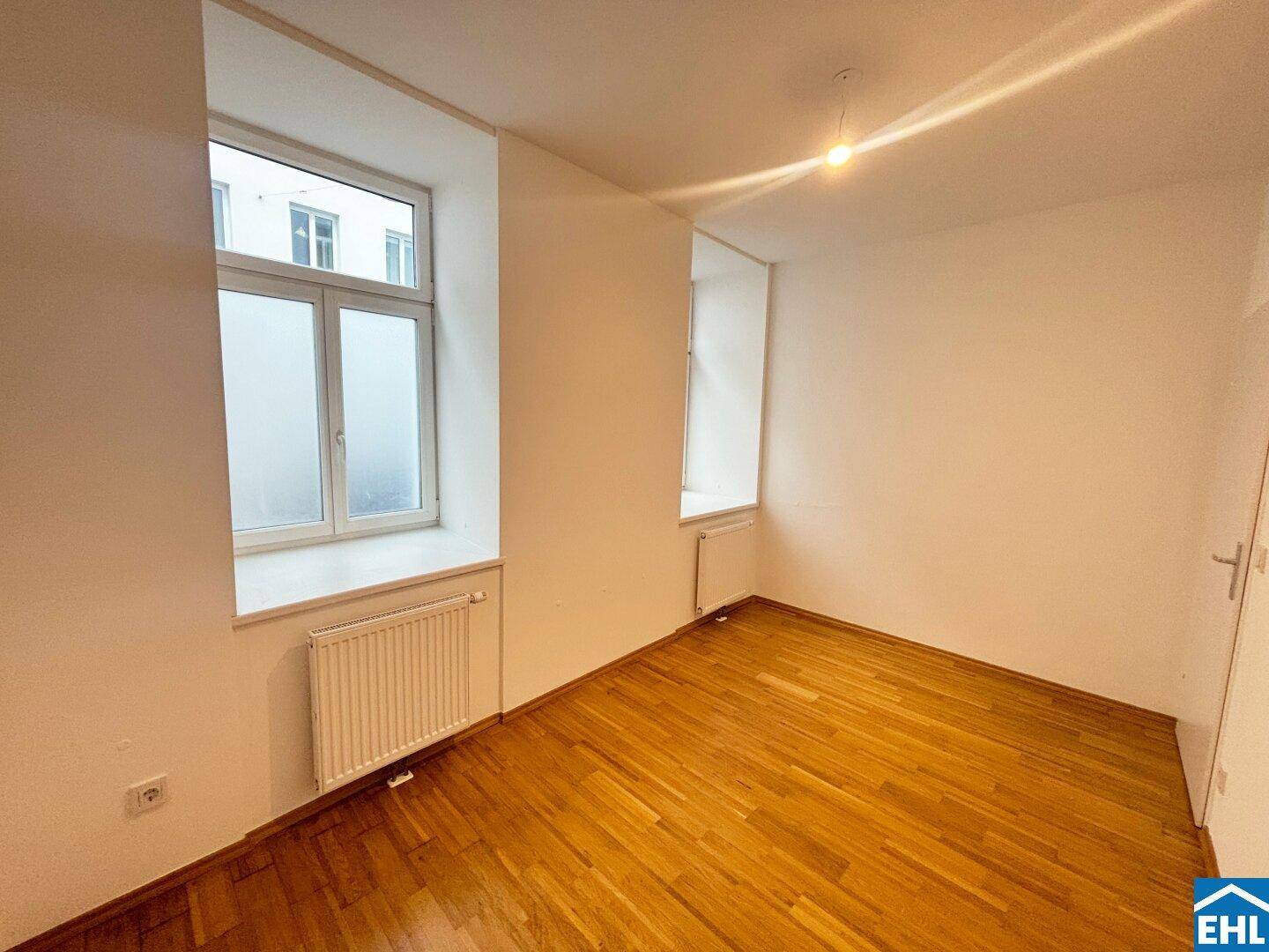 Geräumiges Zimmer mit Holzparkett und zwei Fenstern, bietet viel natürliches Licht.