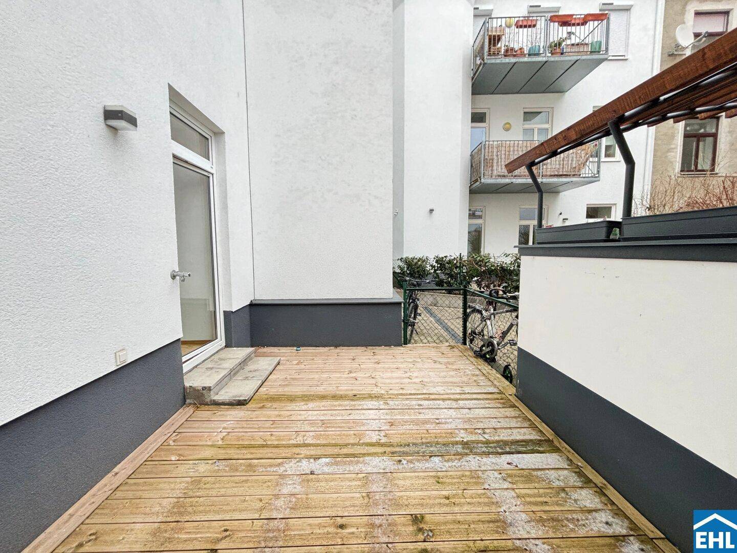 Geräumige Holzterrasse mit Zugang vom Gebäude, ideal für entspannte Stunden im Freien.