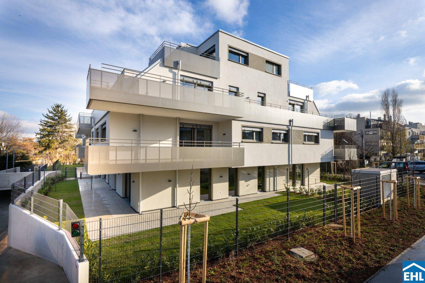 Modernes Mehrfamilienhaus mit klaren Linien, Balkonen und gepflegten Grünflächen unter blauem Himmel.