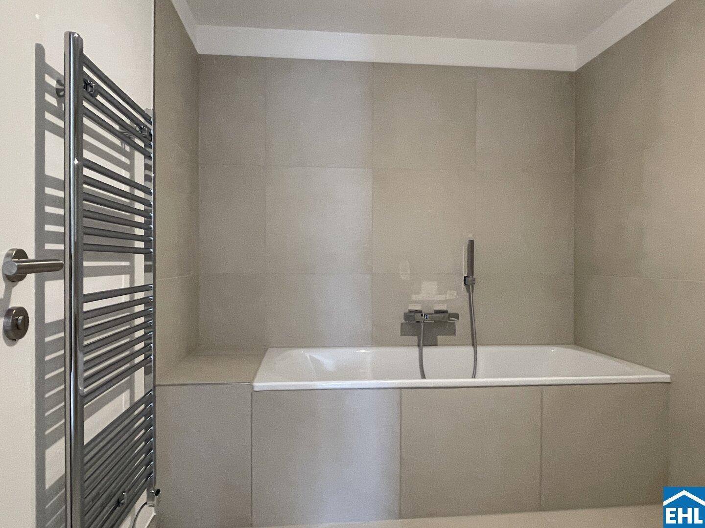 Modernes Badezimmer mit Badewanne, beheiztem Handtuchhalter und hellen Fliesen.
