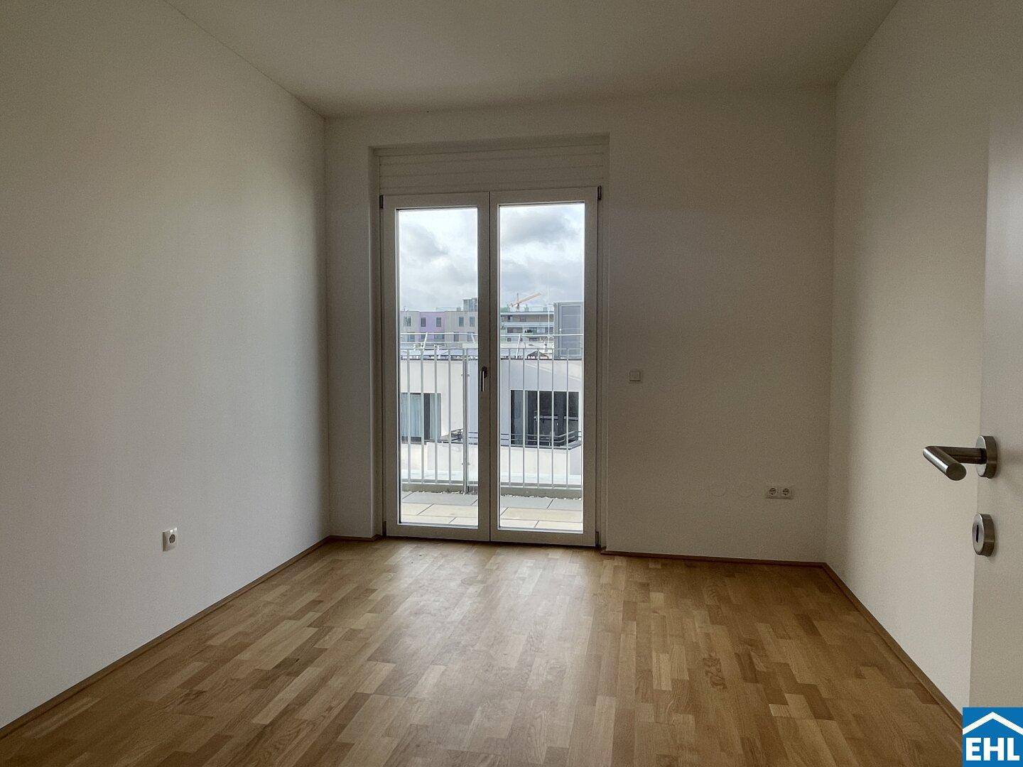 Heller, leerer Raum mit Holzboden und großen Fenstern, die viel Tageslicht hereinlassen.