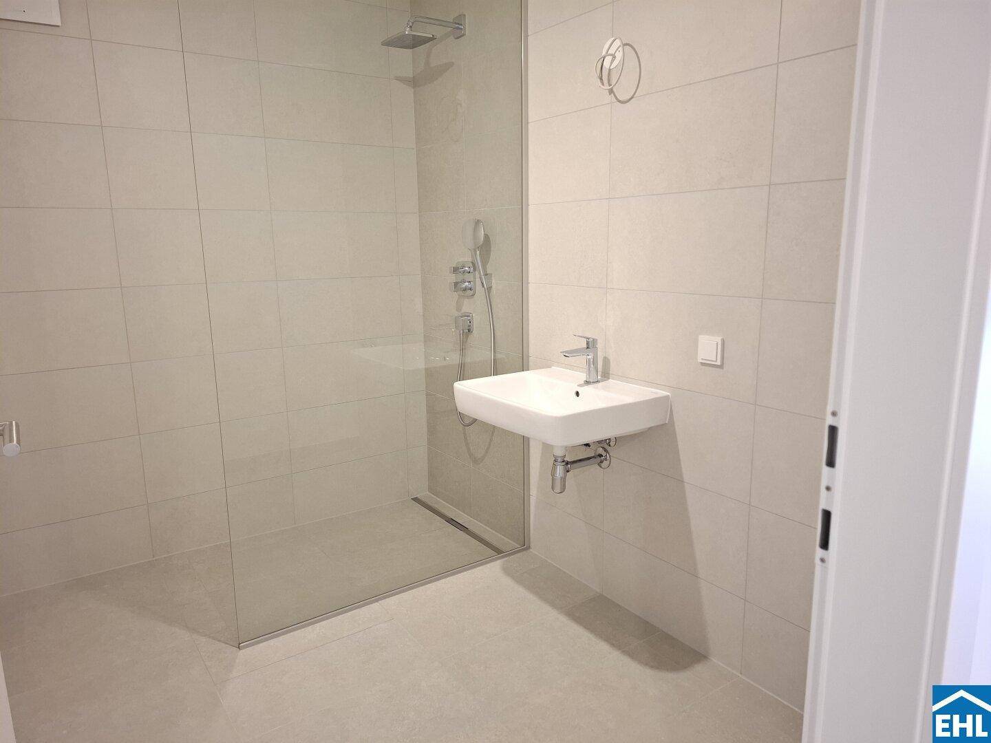 Modernes Badezimmer mit ebenerdiger Dusche, Wandwaschbecken und hellen Fliesen.