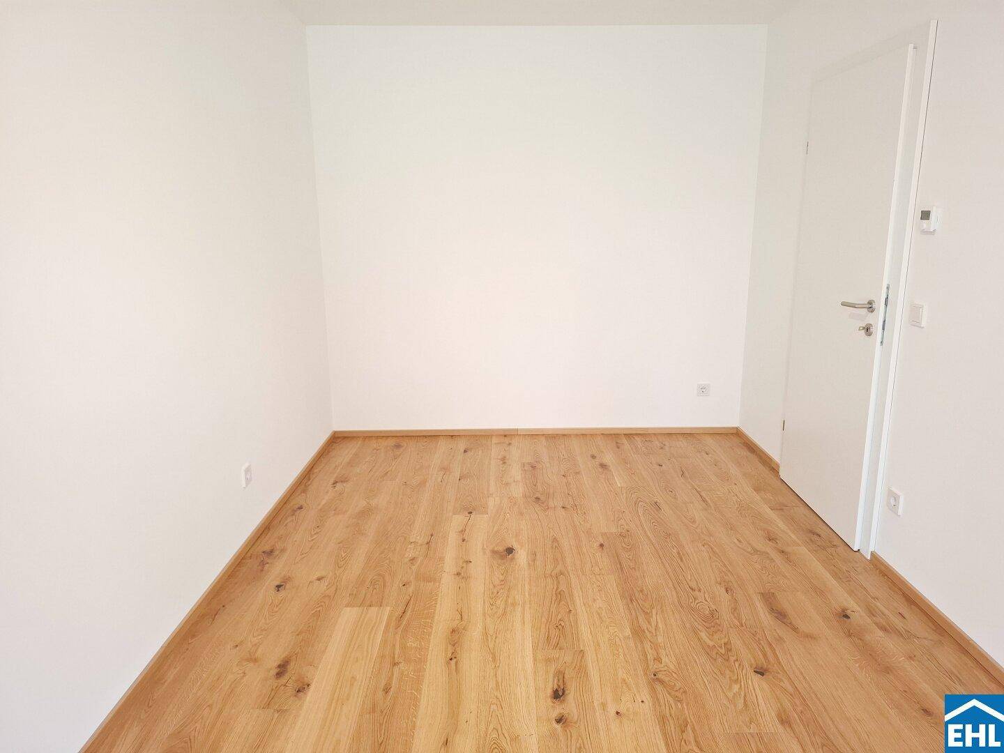 Schlichter, heller Raum mit Eichenparkett und weiß gestrichenen Wänden.