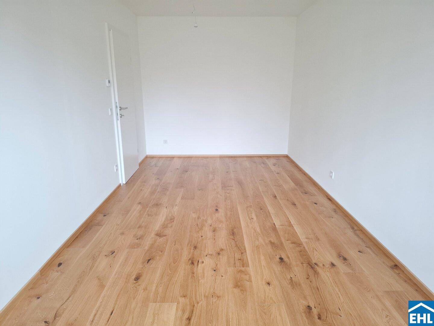 Unmöblierter Raum mit hellem Parkettboden und weißer Tür, ideal als Schlafzimmer.