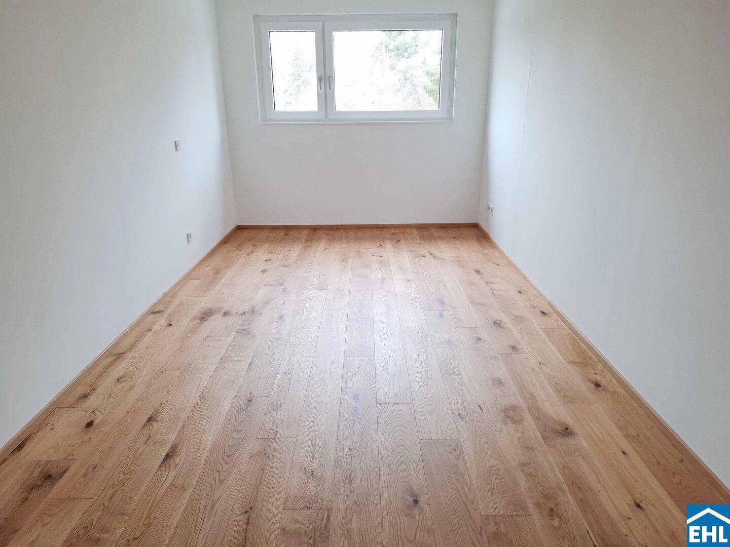 Unmöblierter Raum mit Holzboden und Fenster, bietet viel natürliches Licht.