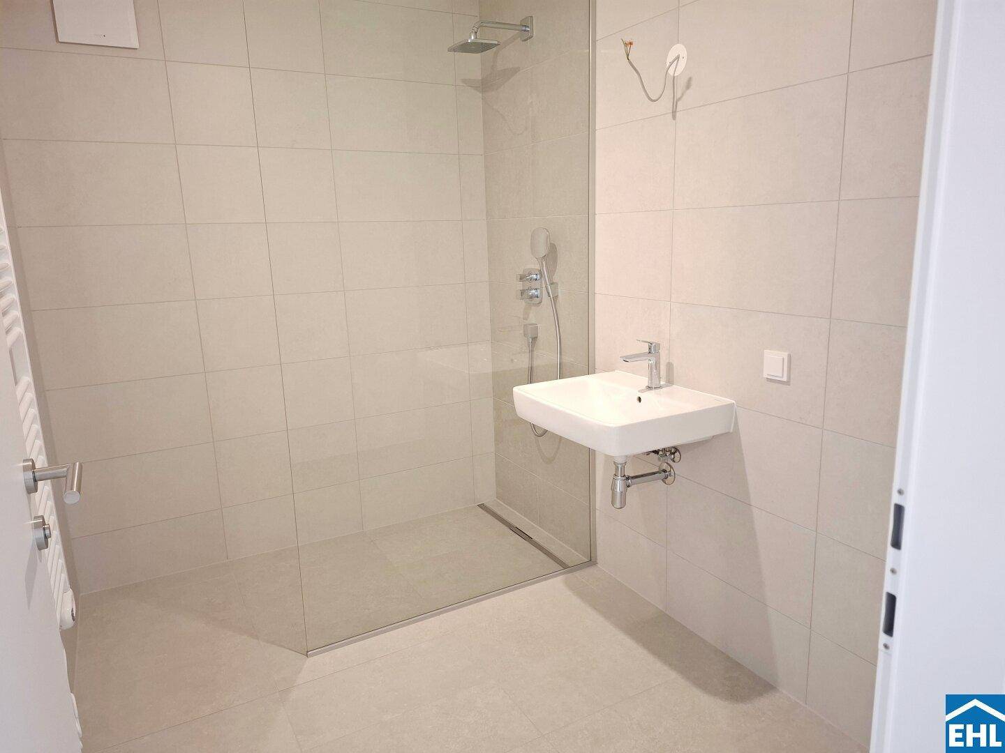 Modernes Badezimmer mit begehbarer Dusche, Wandwaschbecken und hellen Fliesen.