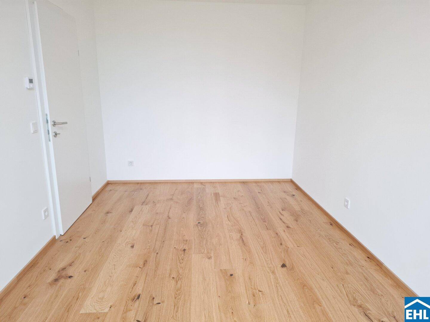 Schlichter, heller Raum mit Holzboden und weiß gestrichenen Wänden, ideal als Schlaf- oder Arbeitszimmer.