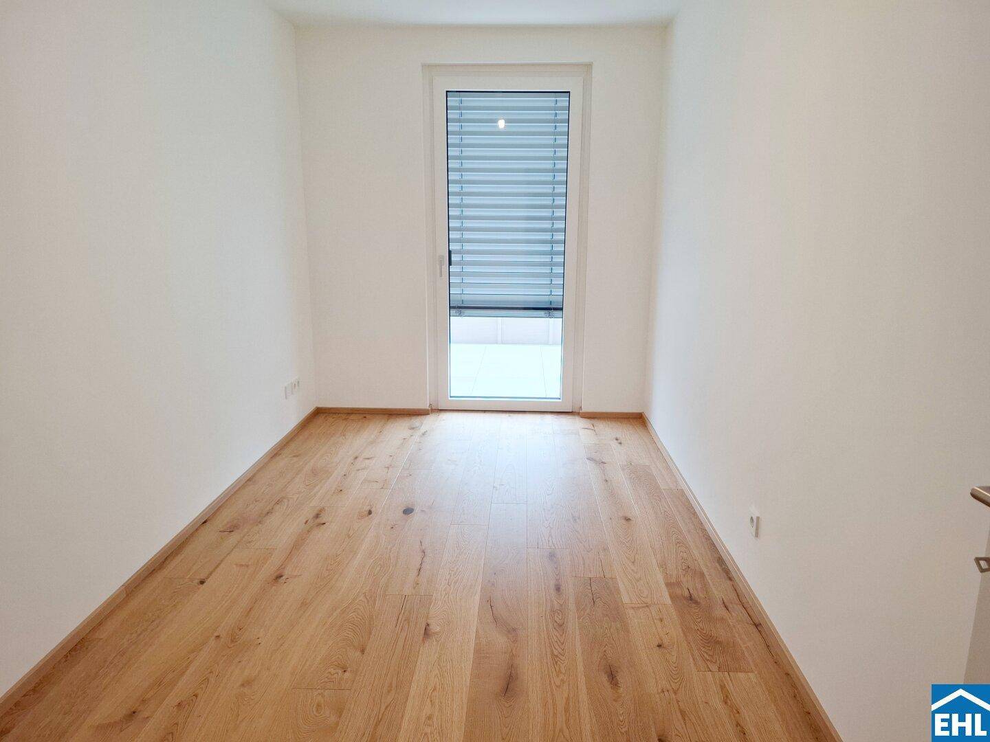 Leerer Raum mit Holzboden und Fenster mit Jalousien für Privatsphäre.