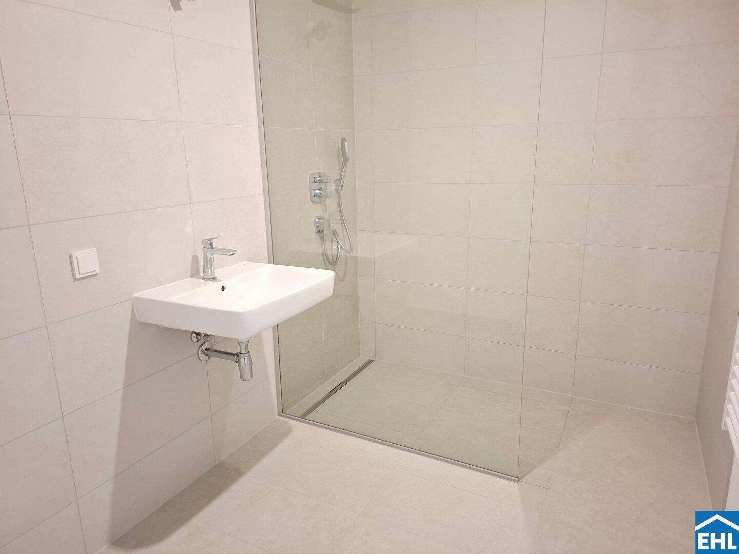 Modernes Badezimmer mit ebenerdiger Dusche, Wandwaschbecken und hellen Fliesen in zeitgemäßem Design.
