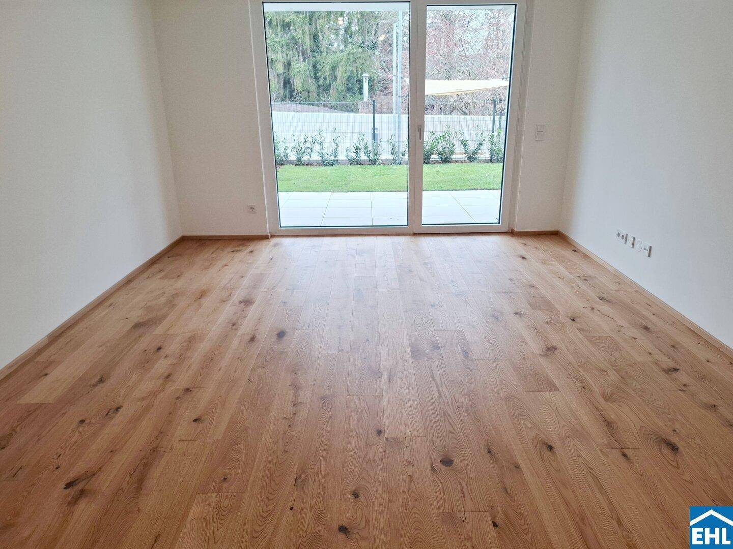Lichtdurchfluteter Raum mit Holzboden und großen Fenstern, die Zugang zum Außenbereich bieten.