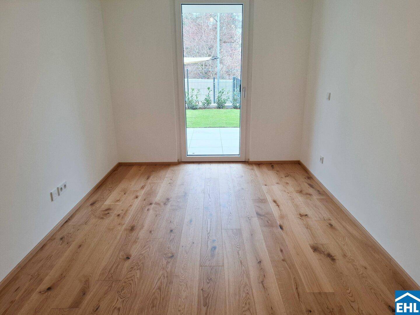 Helles Zimmer mit Holzboden und einer Tür, die zum Garten oder zur Terrasse führt.